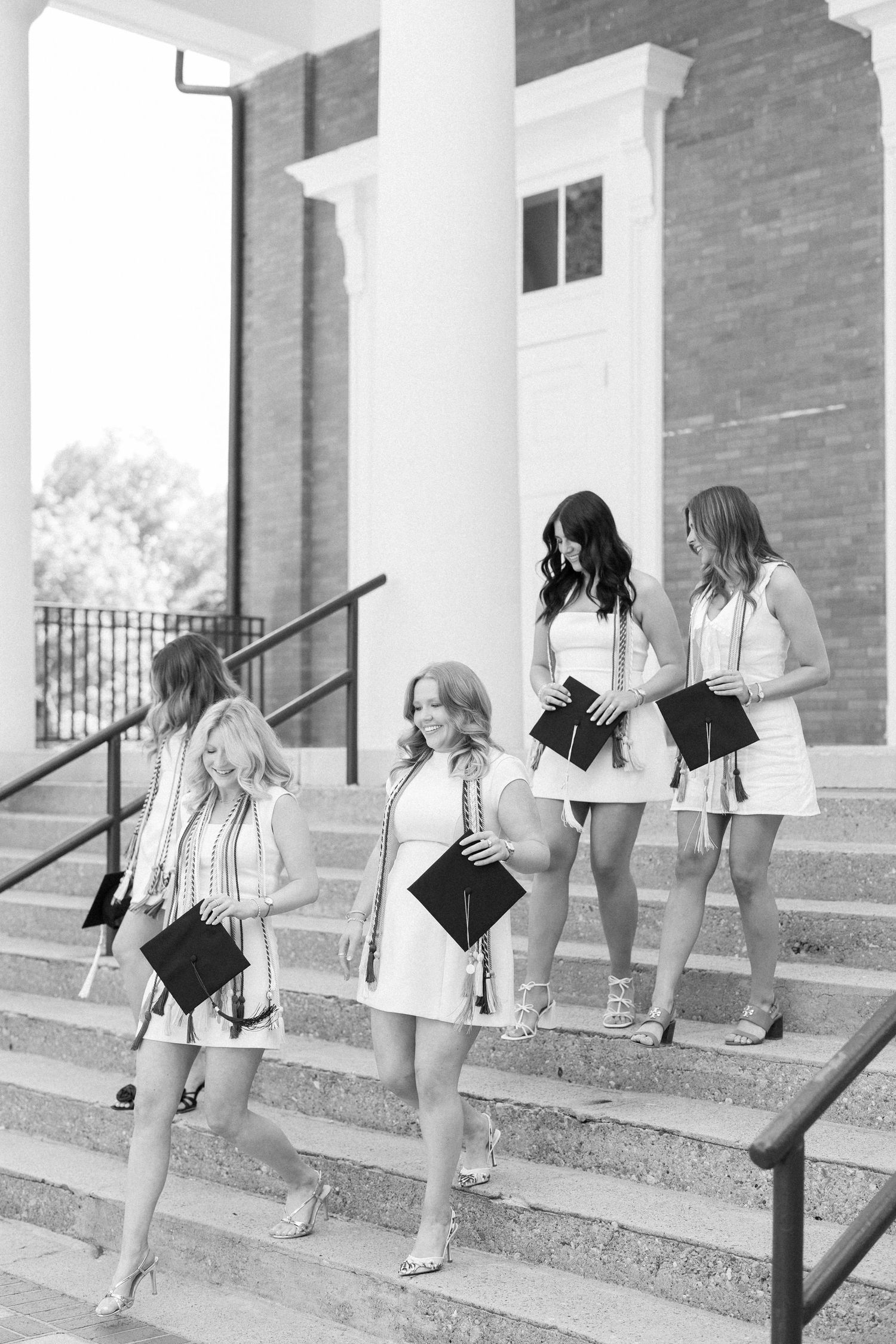A sequence of black and white photos showing people playfully descending steps while holding graduation caps.