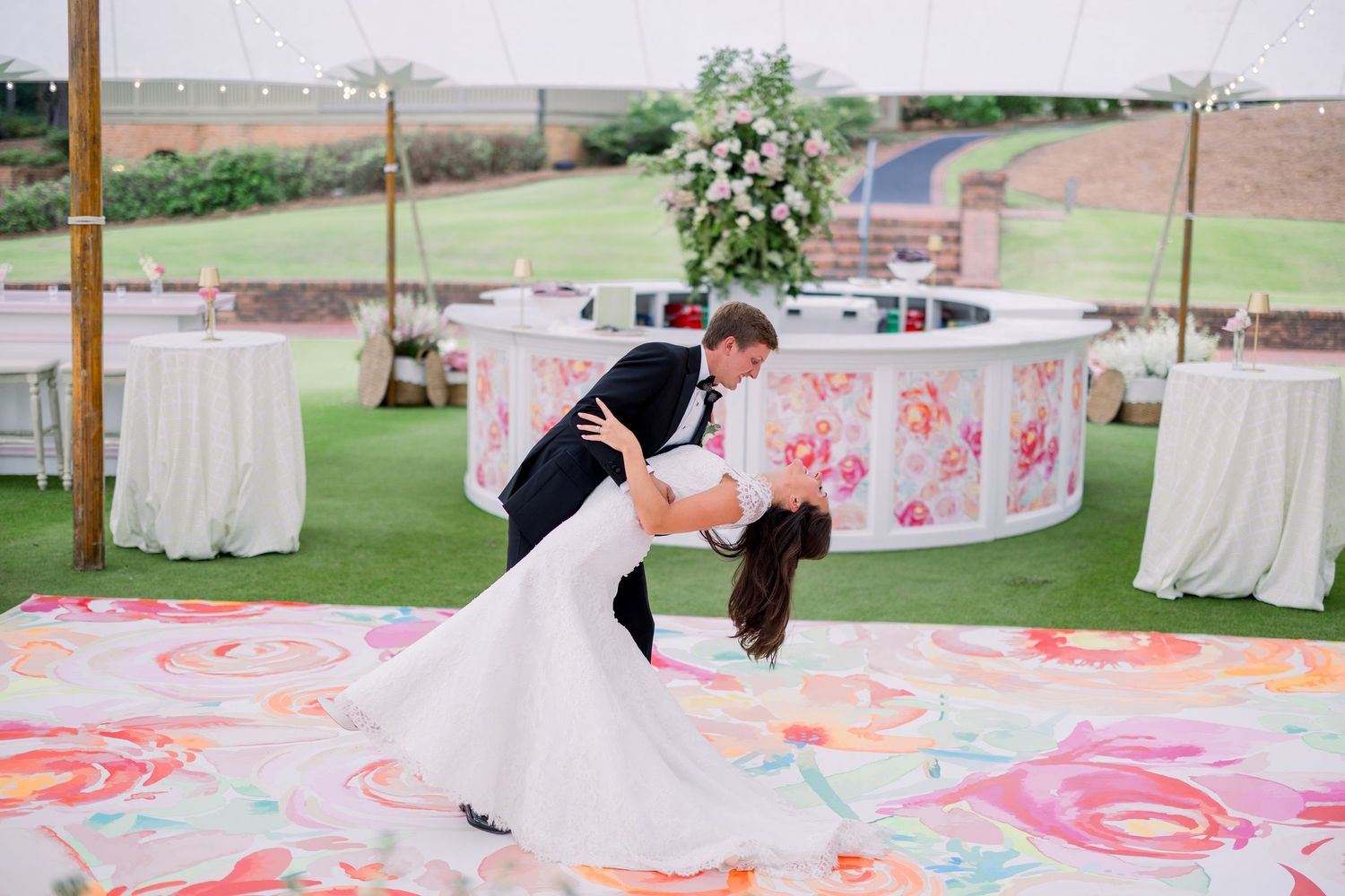 A romantic dip dance on a floral patterned dance floor at an outdoor wedding reception.