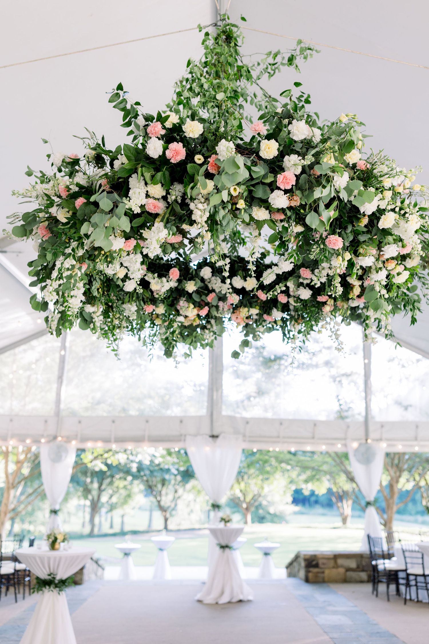 Lush floral chandelier with pink and white roses, greenery, hanging under a white wedding tent.
