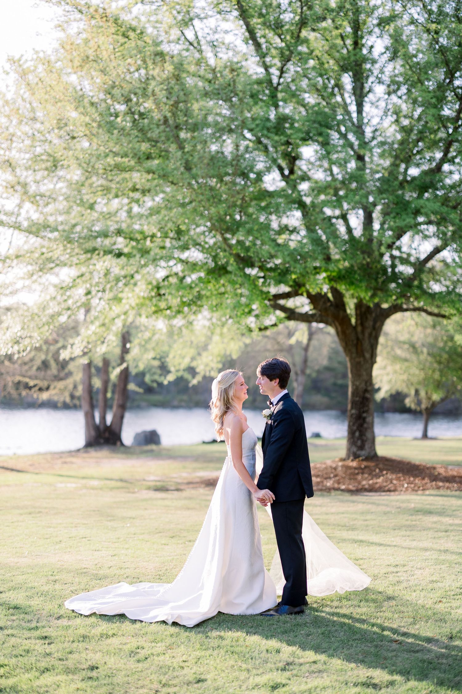 Wedding couple shares intimate moments on a grassy hillside under mature trees.