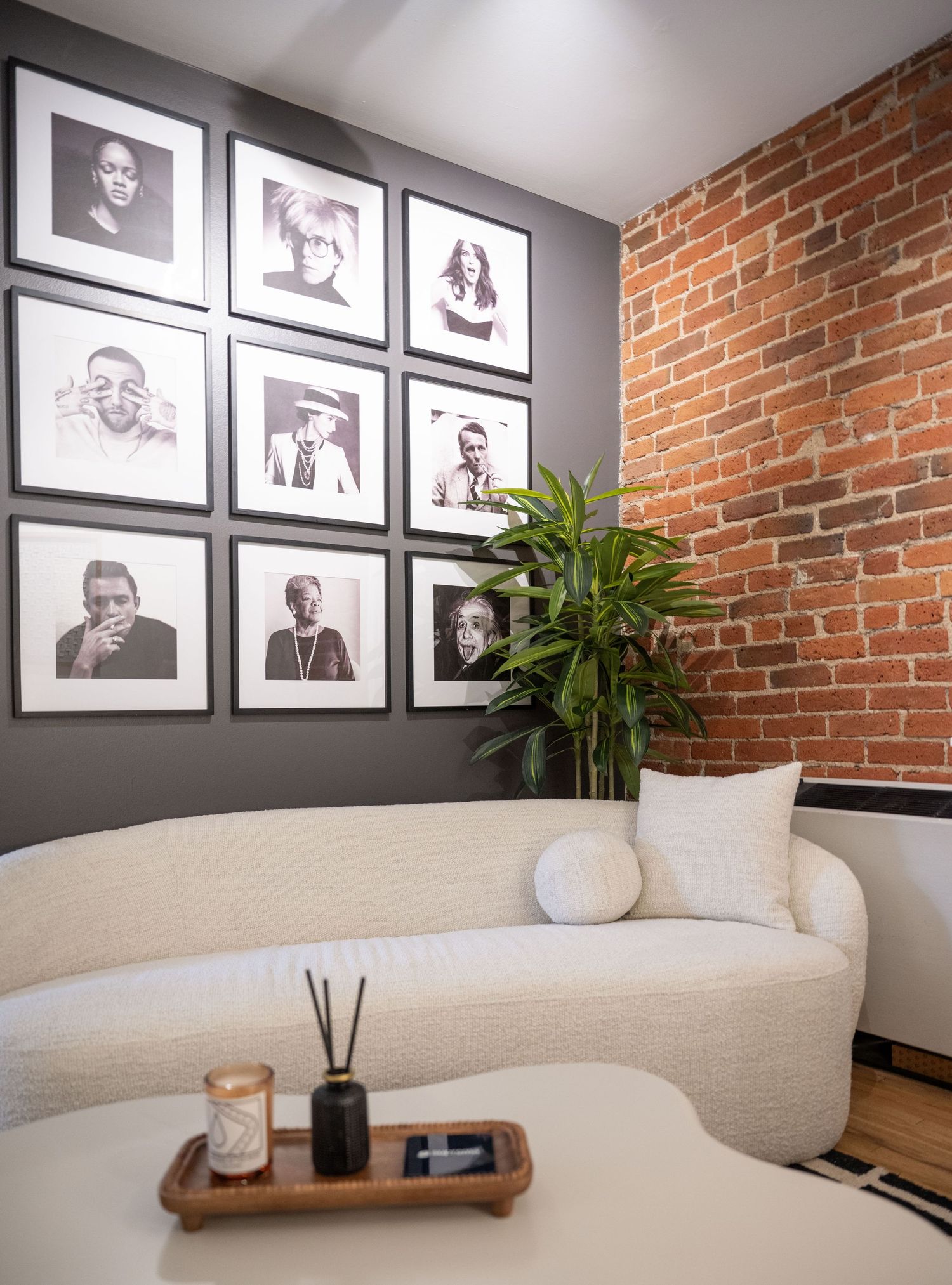 Stylish office lounge with exposed brick wall, framed artwork, and curved white sofa.