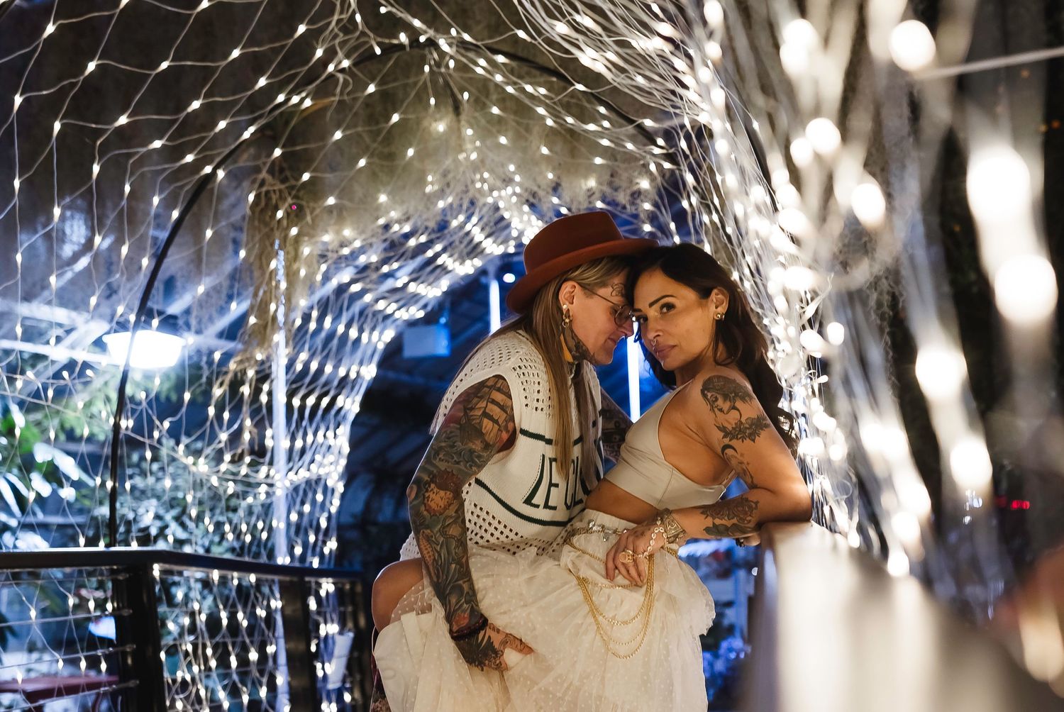 Tattooed couple embracing romantically under a sparkling fairy light tunnel installation.