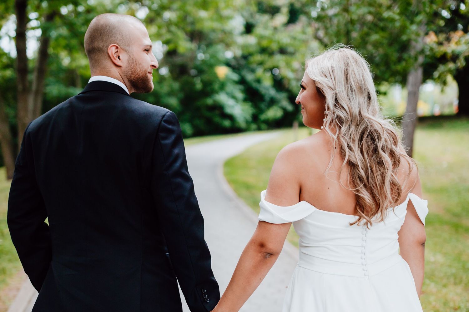 Couple walking through a lush garden pathway during a wedding photoshoot.