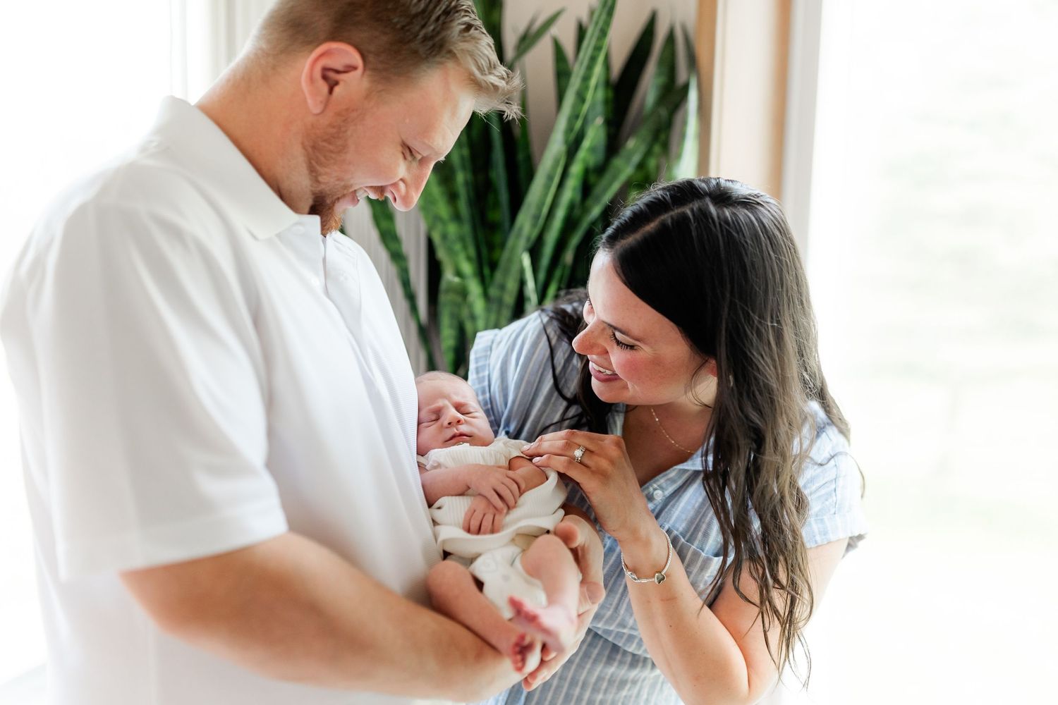 Intimate lifestyle photos of couple with newborn baby in bright interior setting.