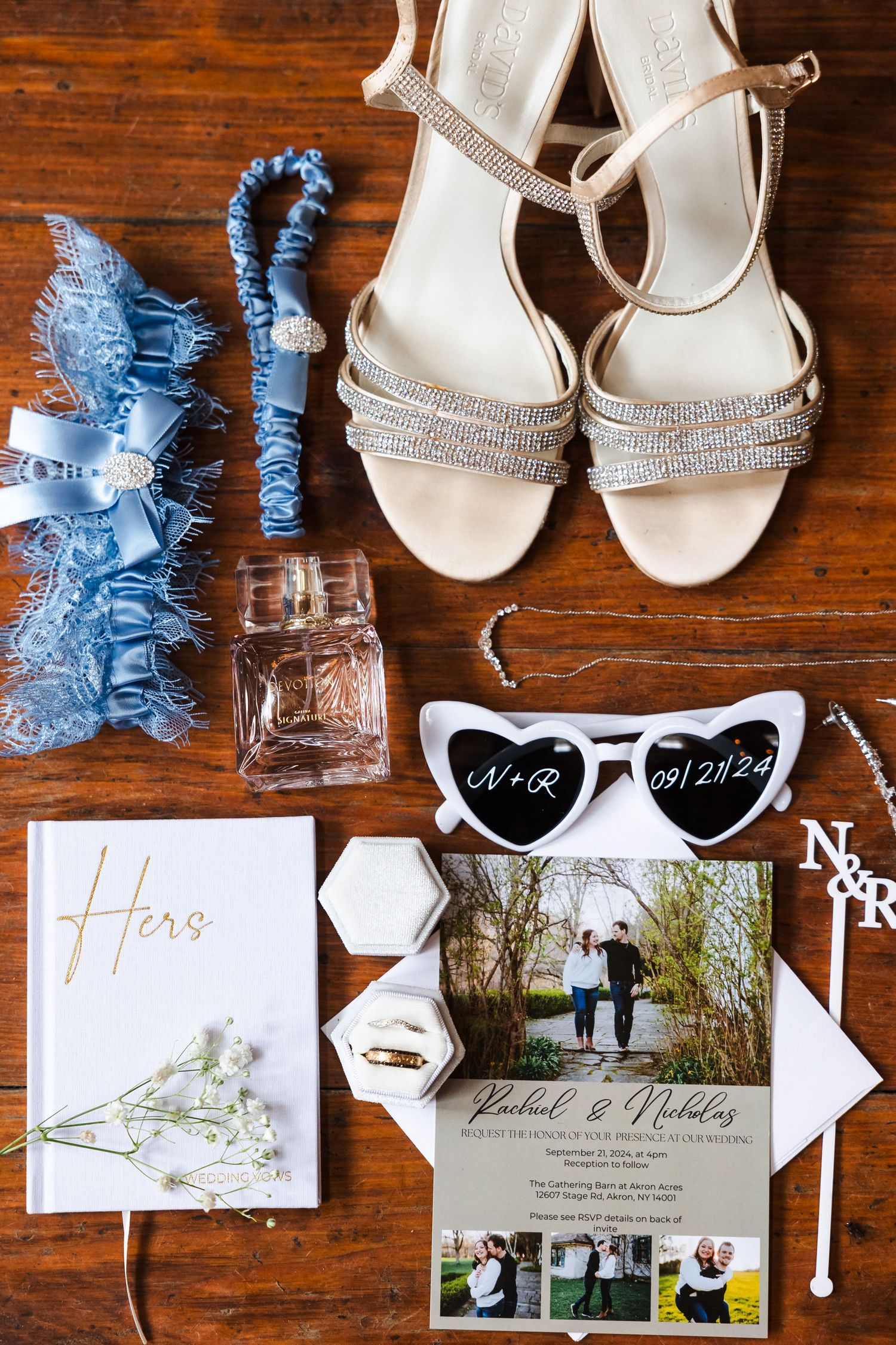 Wedding details flatlay with blue garter, crystal shoes, and invitation suite on wooden background.