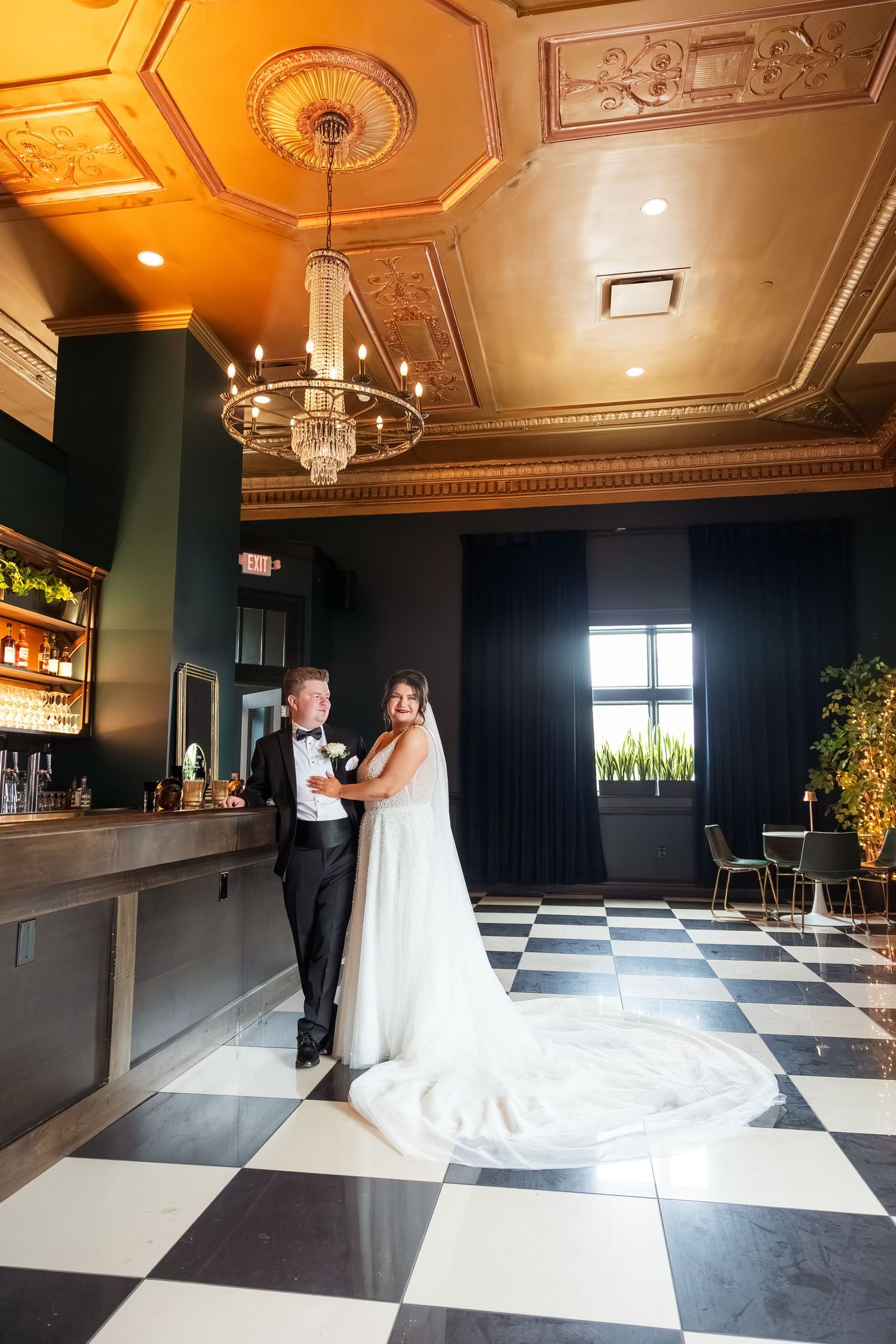 Elegant ballroom with checkerboard floor and ornate gold ceiling for wedding reception.