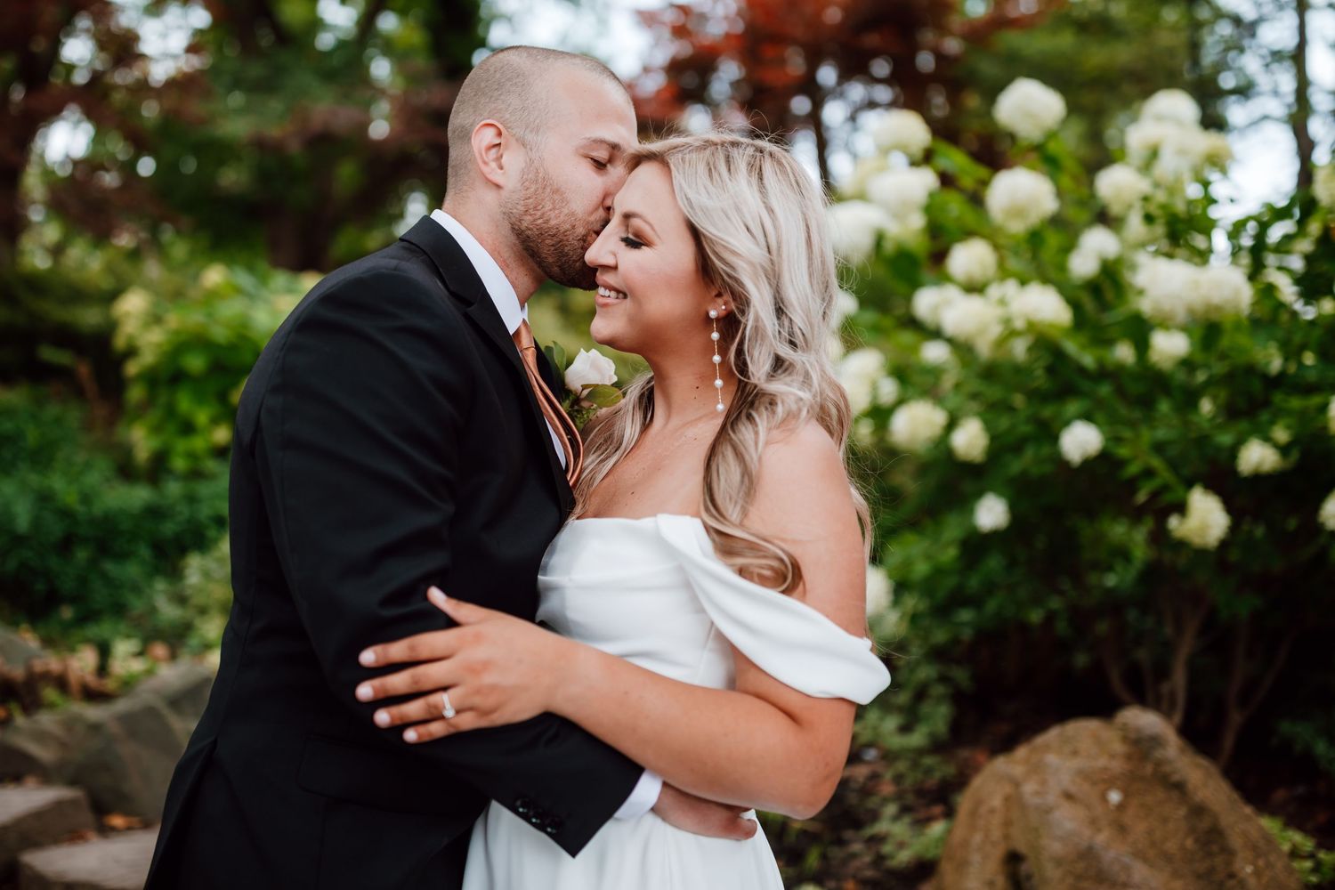 A romantic wedding moment captured in a garden setting with white hydrangea blooms in the background.