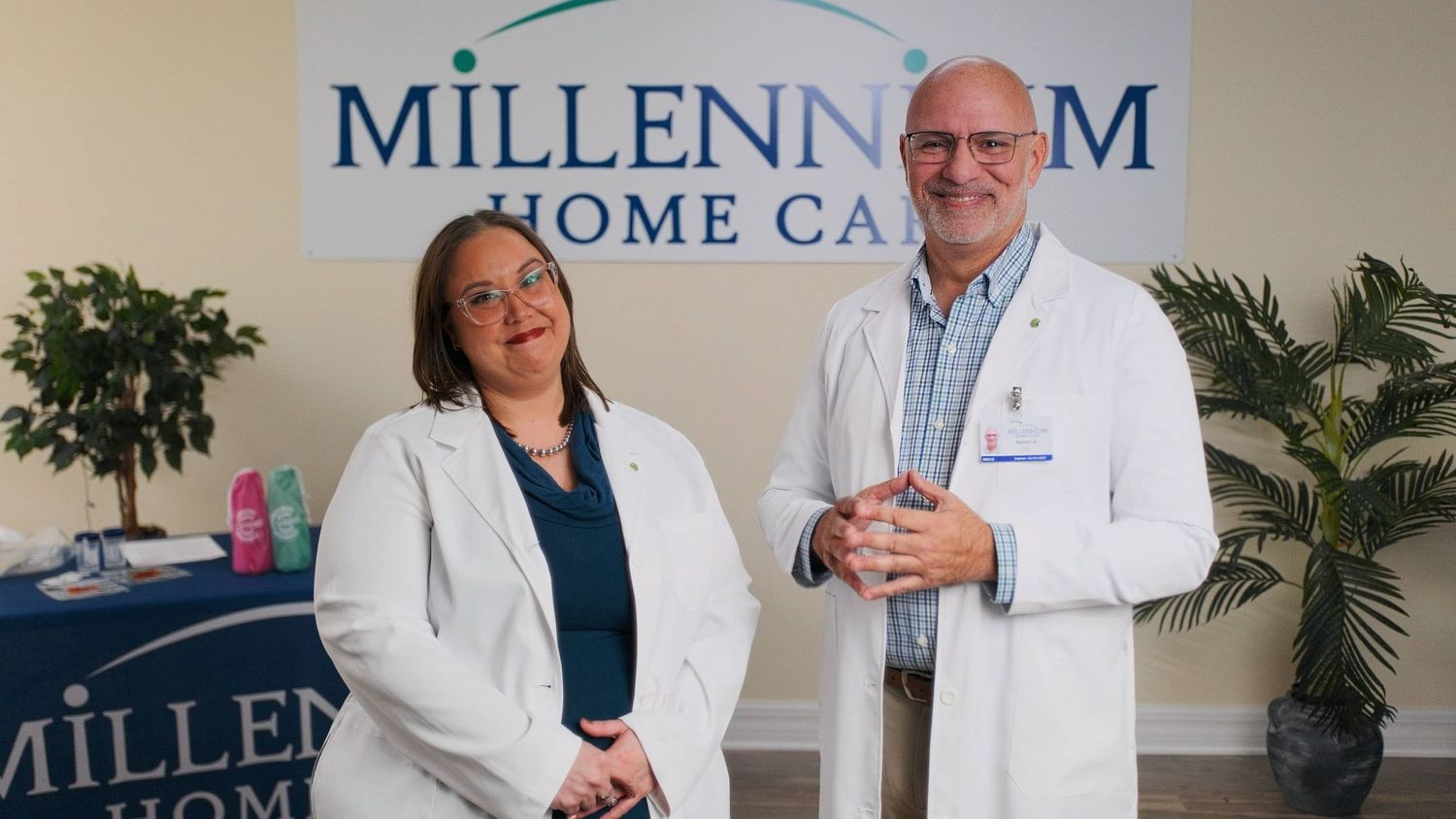 Two healthcare professionals in white coats smile at Millennium Home Care office.