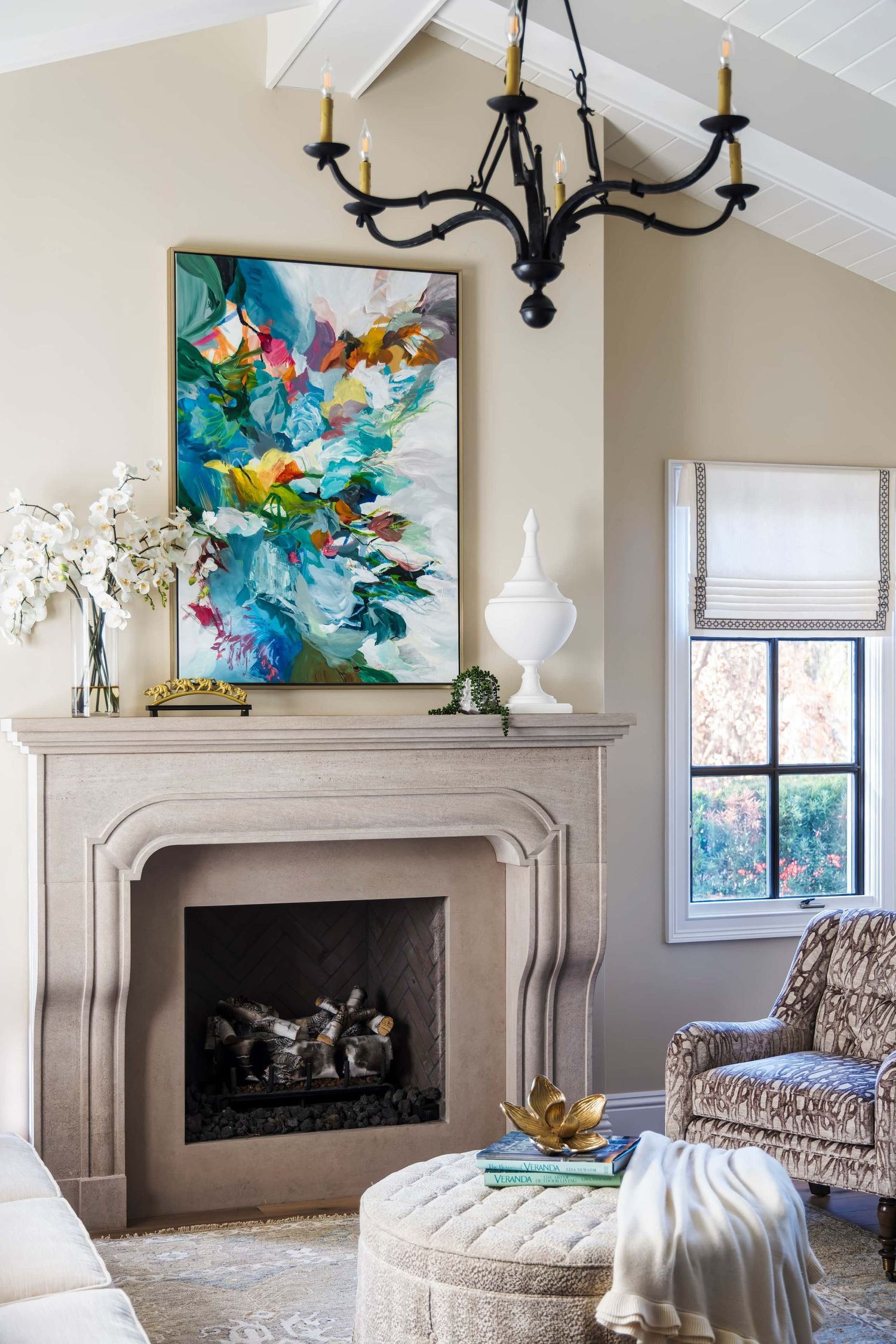Elegant living room with a stone fireplace, colorful abstract painting, black chandelier, and neutral decor accents.
