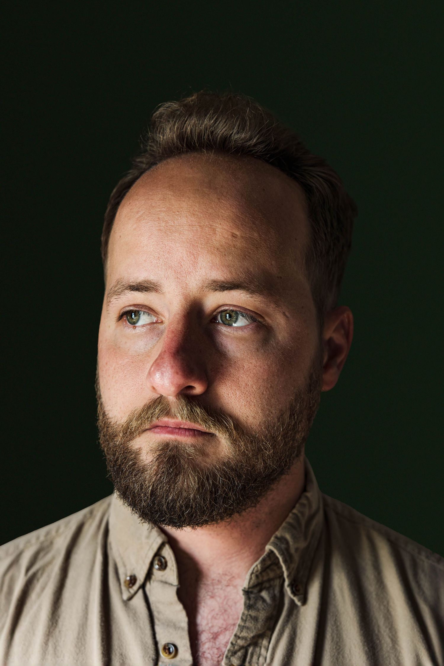 Dramatic portrait lighting on bearded man against dark green background.