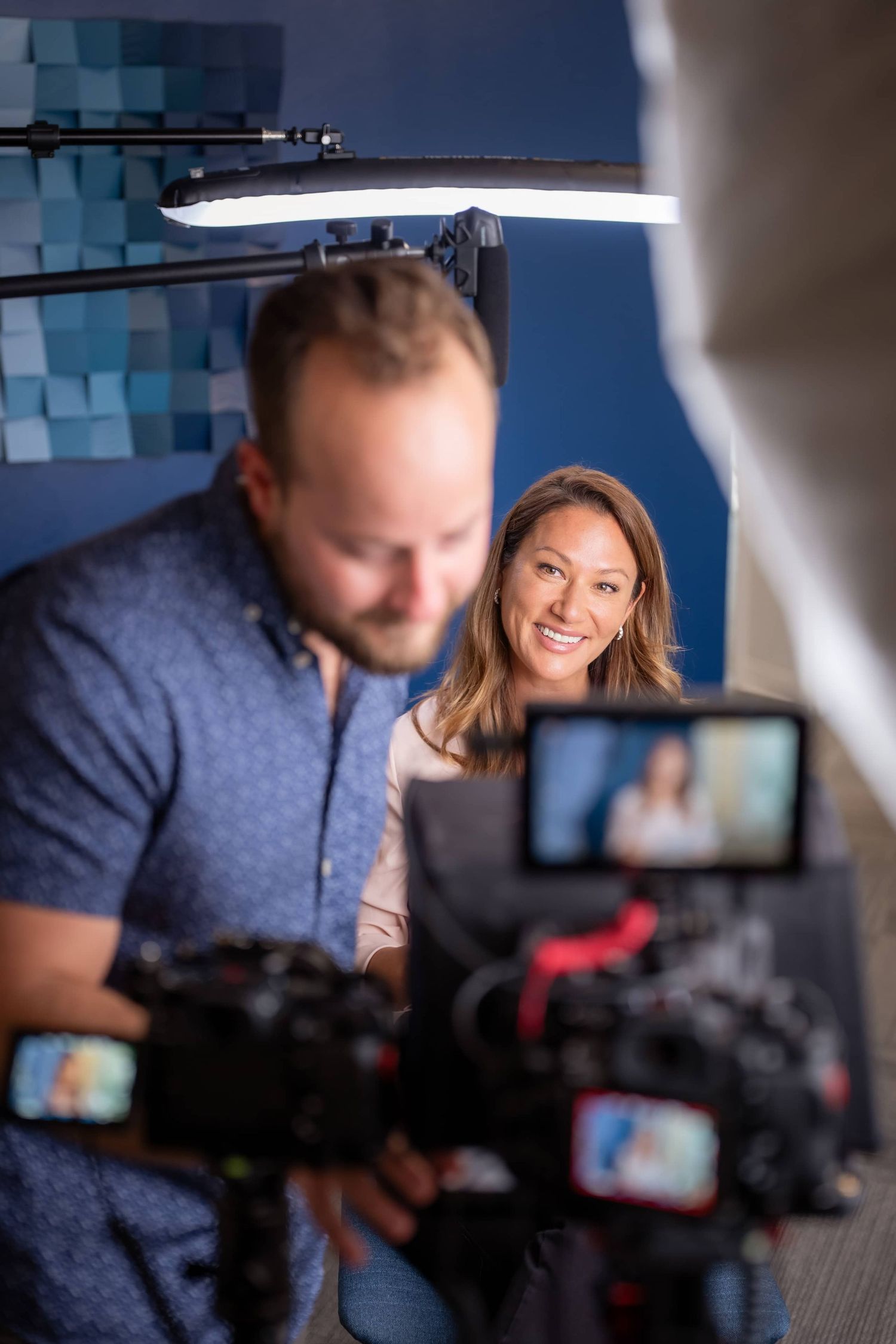 A smiling female CEO being filmed in a professional video studio setup with camera equipment and bright lighting.
