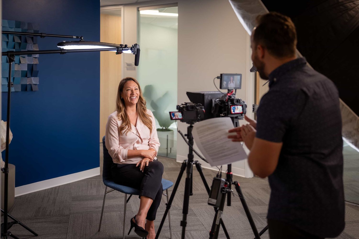 A woman being interviewed on camera in a professional studio setting with blue walls and studio lighting equipment.