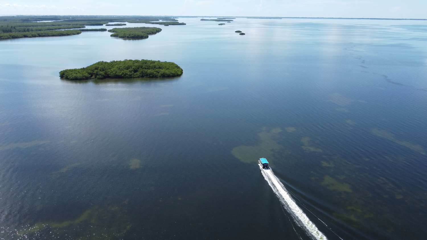 Aerial view of small boat navigating through Florida waterways with mangrove islands and turquoise waters.