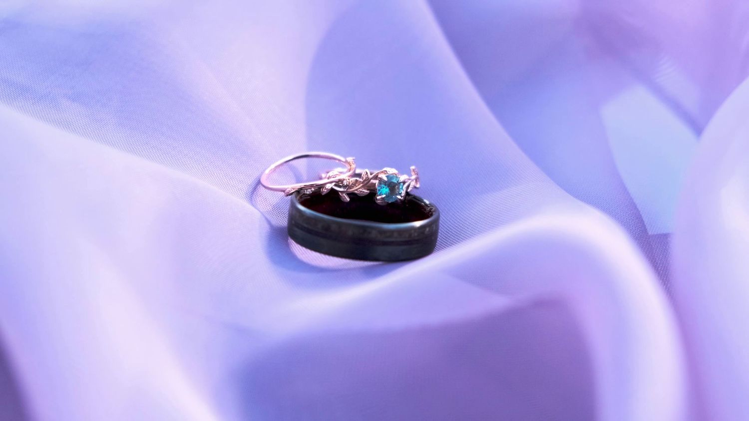 Elegant wedding rings displayed on black surface against soft purple fabric background.
