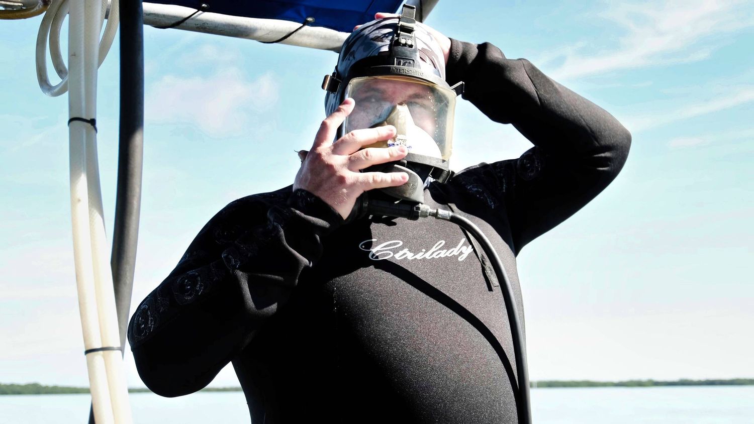 Activist in a dive suit putting on a dive mask on boat against bright sky.