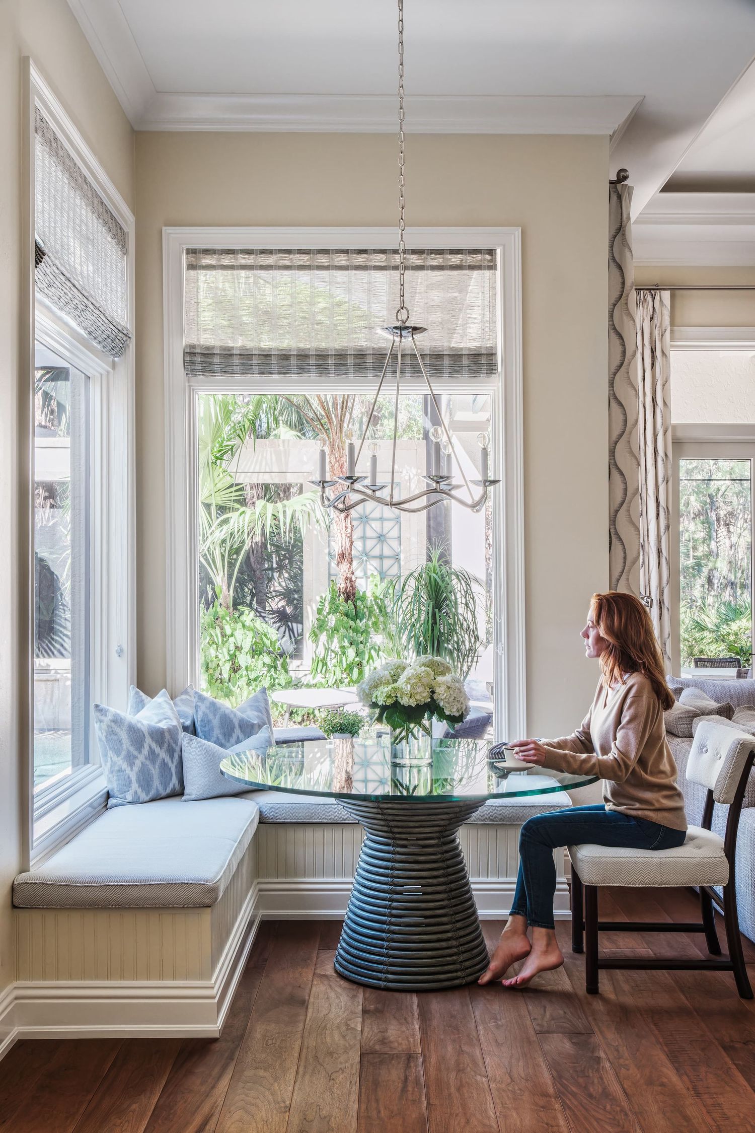 Bright breakfast nook with built-in bench seating and round table next to large window overlooking garden.