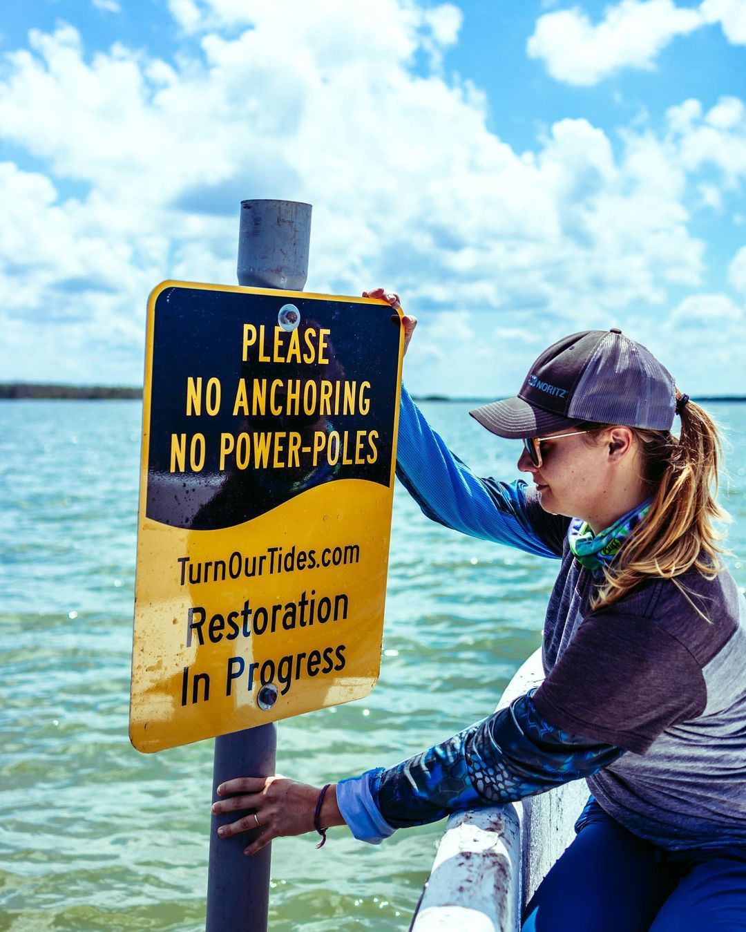 No anchoring or power poles warning sign on waterfront with restoration project information.