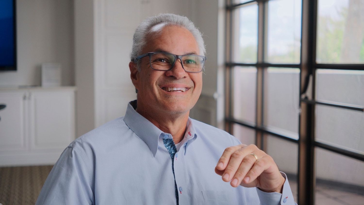 Smiling medical executive with glasses wearing a light blue shirt in a bright modern room.