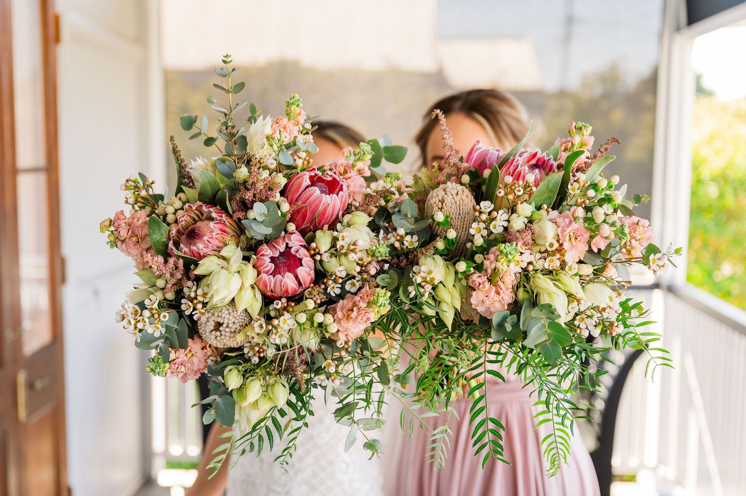 Lush floral arrangement with pink and white blooms mixed with greenery on a bright windowsill.