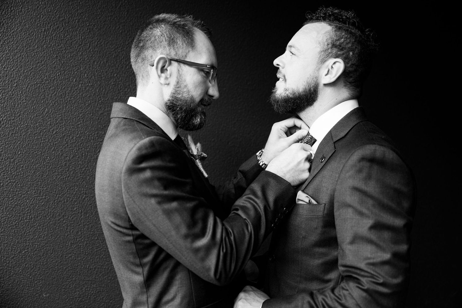 Black and white portrait of two people adjusting formal ties before a wedding ceremony.