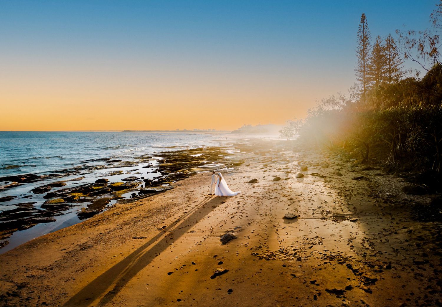 Silhouette walking along rocky coastal beach during golden sunset.