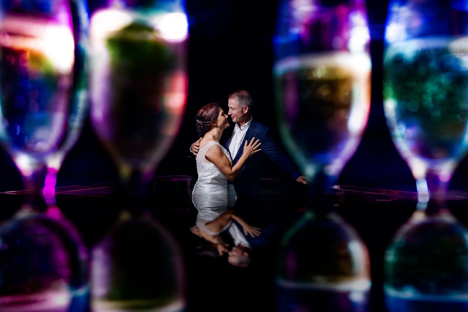 Creative wedding photo with couple silhouetted against colorful champagne glass bokeh.