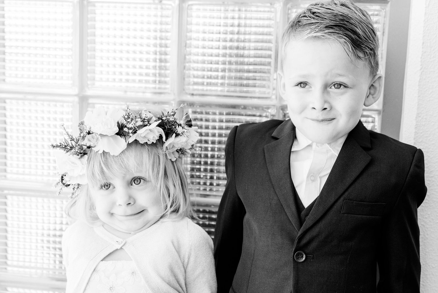 Black and white portrait of two young children in formal attire, one wearing a floral crown.
