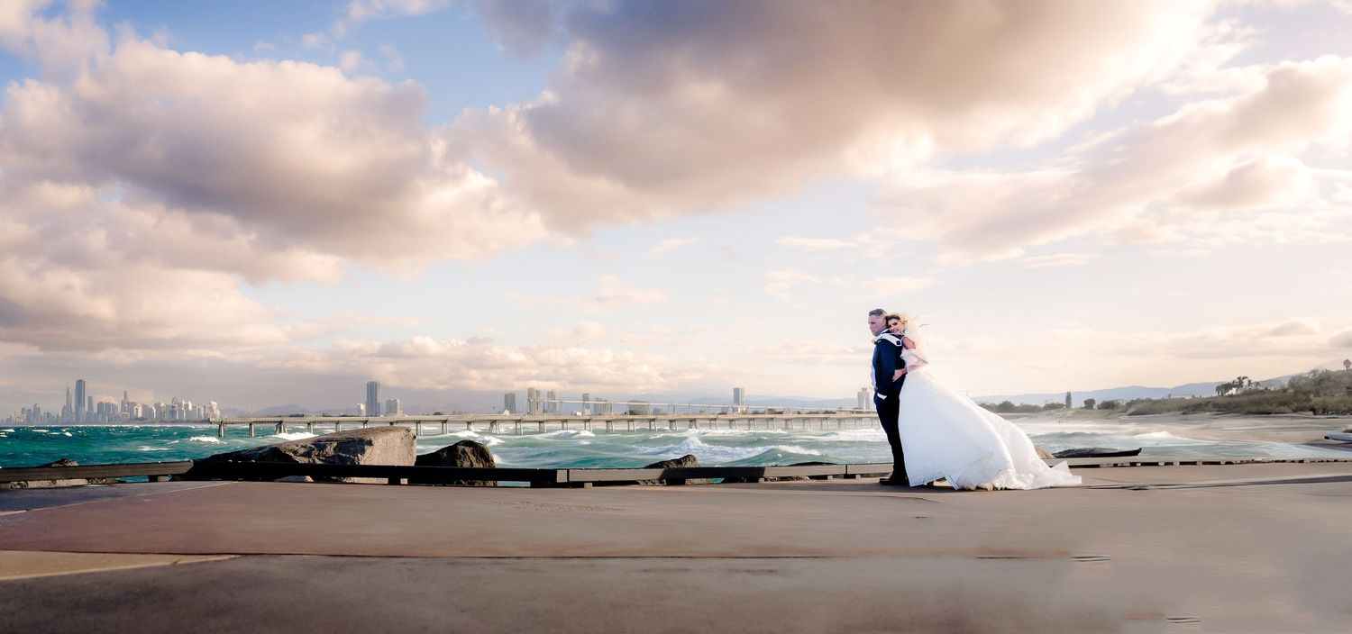 A scenic wedding portrait silhouetted against a dramatic cloudy harbor skyline.