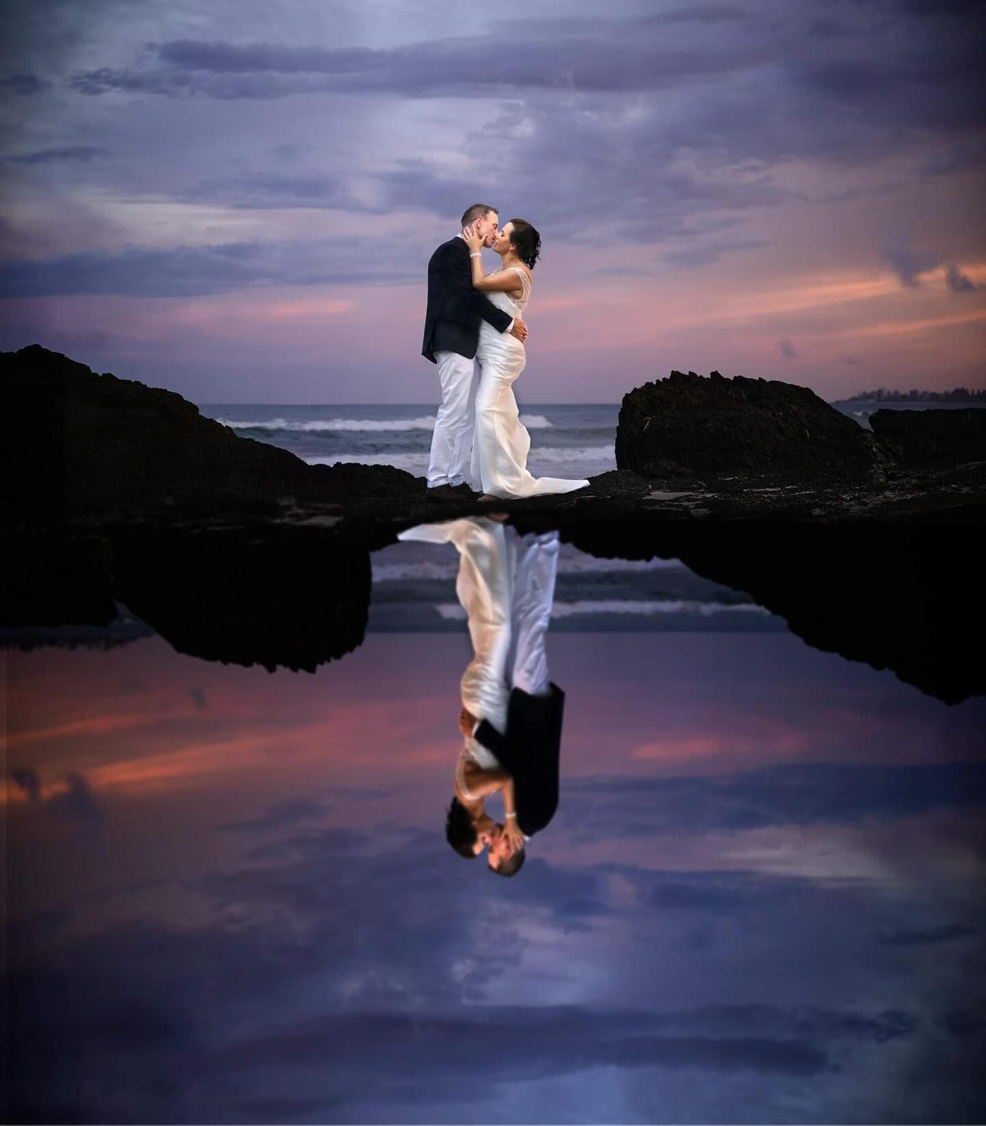 Romantic couple reflected in tide pool at sunset with dramatic coastal landscape.