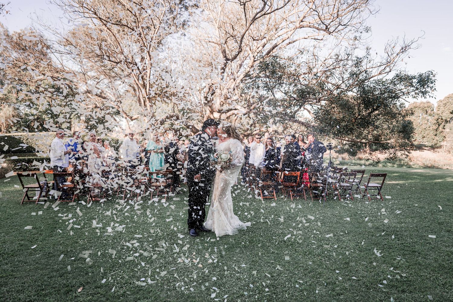 Wedding couple surrounded by confetti shower during outdoor celebration.