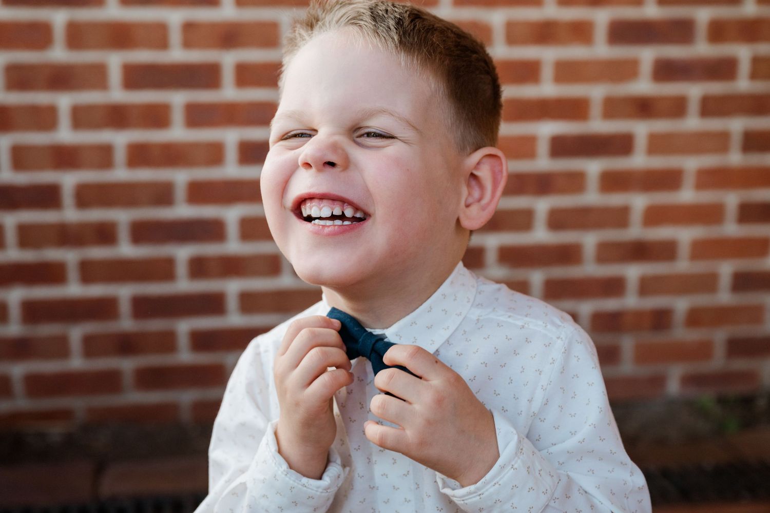 Young boy in white shirt adjusting his bow tie while laughing.