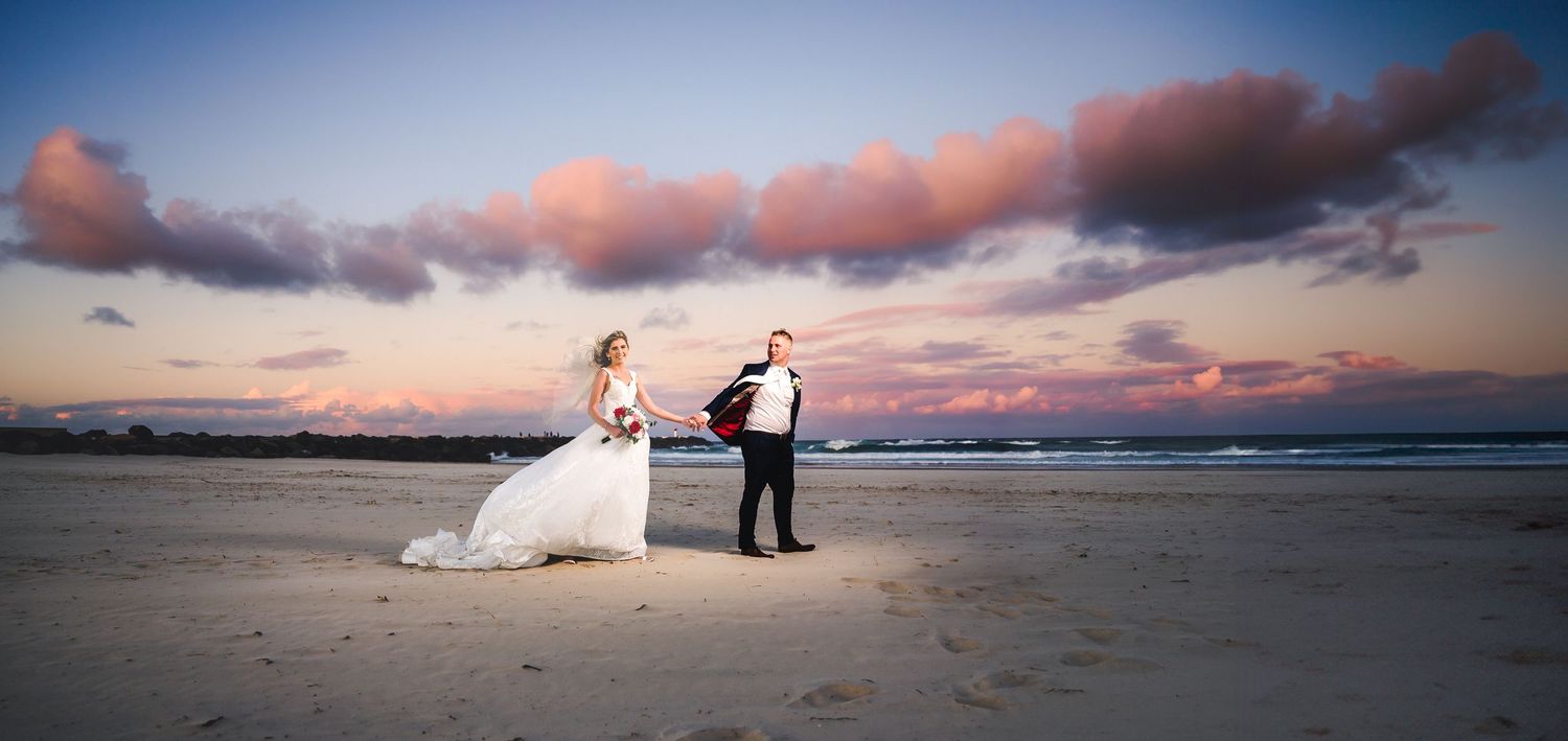 Wedding couple on beach at sunset with dramatic pink clouds.