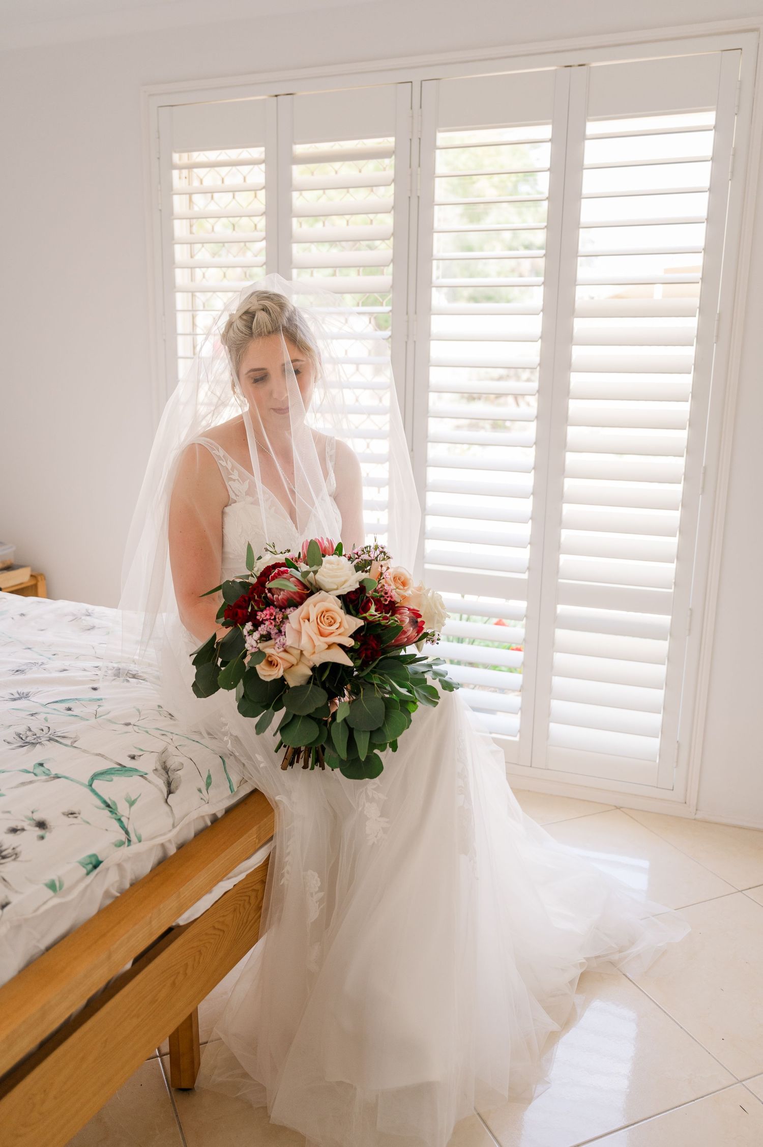 Wedding dress and bouquet with pink and white flowers in a bright room with plantation shutters.