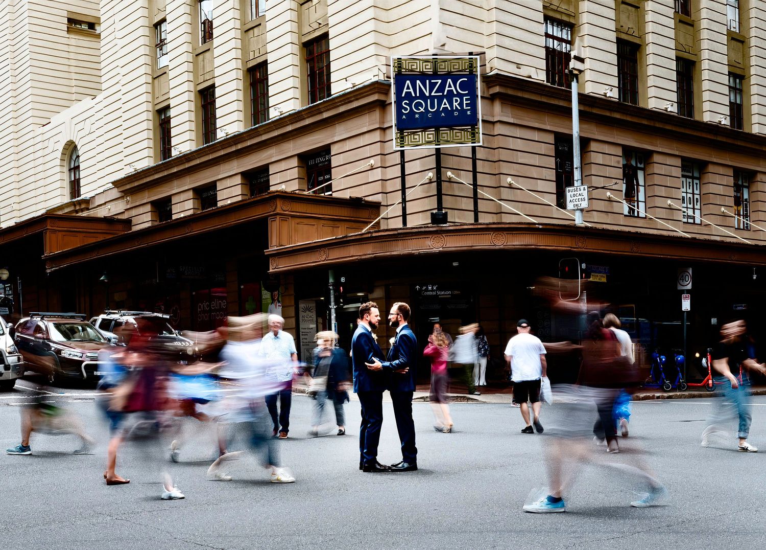 Blur of pedestrians passing by outside a historic building on a busy city street.