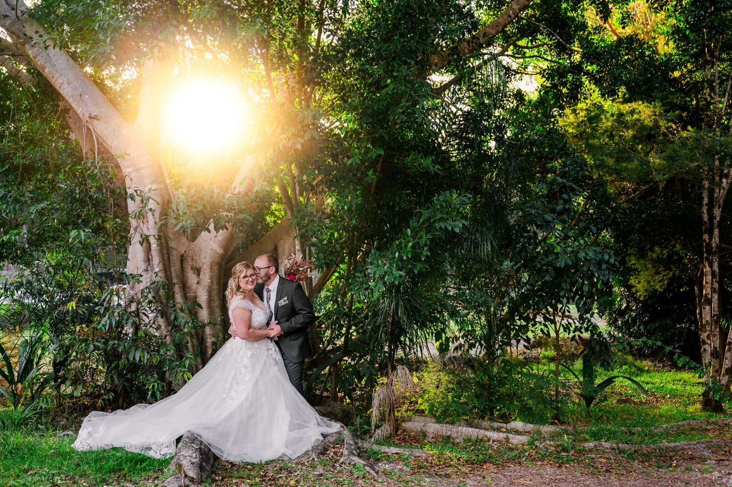 Sunlight streams through trees onto a romantic garden wedding scene.