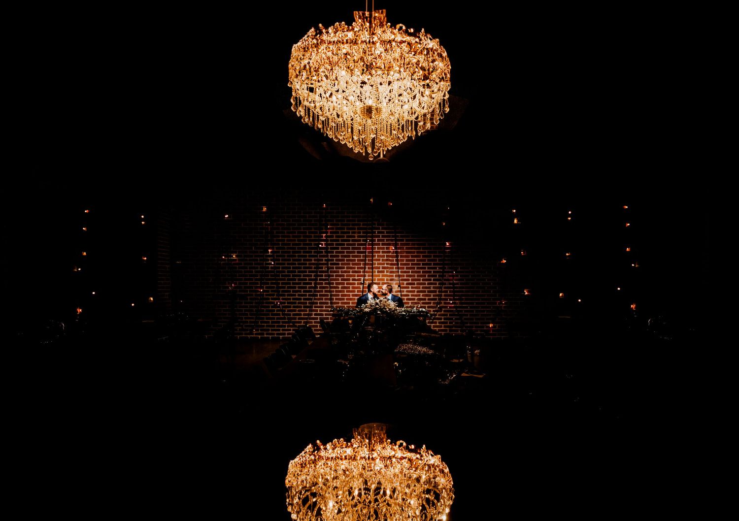 Elegant crystal chandeliers illuminate a dark reception space with dramatic lighting.