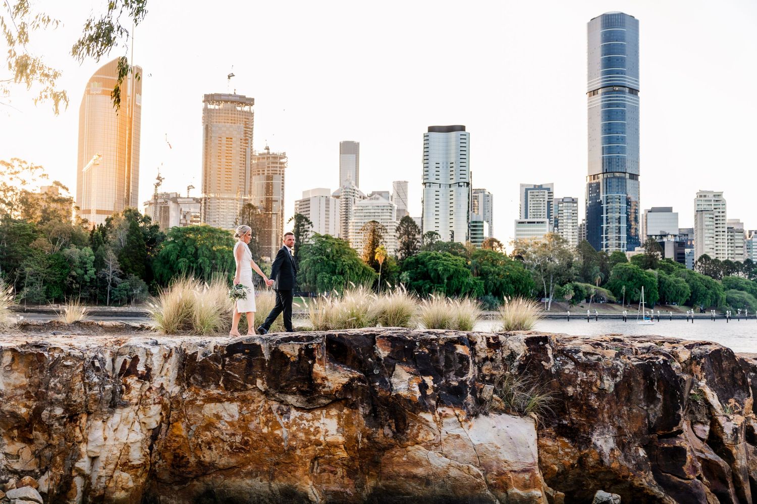Wedding couple silhouetted against Brisbane city skyline at sunset.
