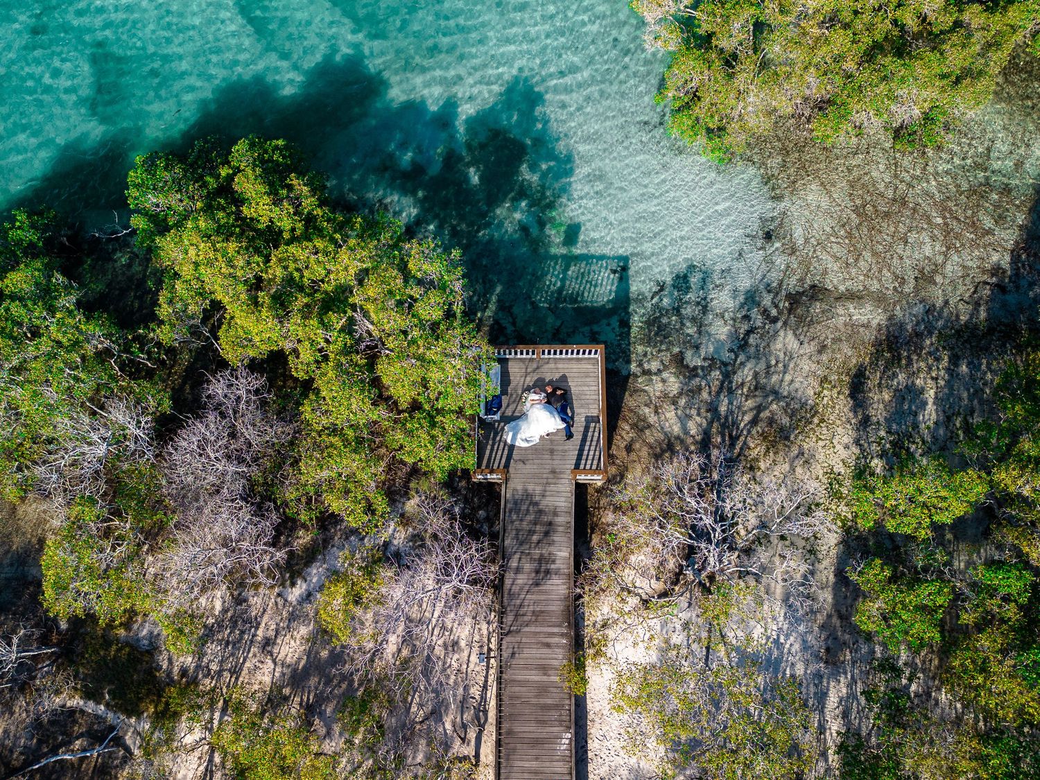 Aerial view of a wedding couple on a wooden pier extending into turquoise waters.