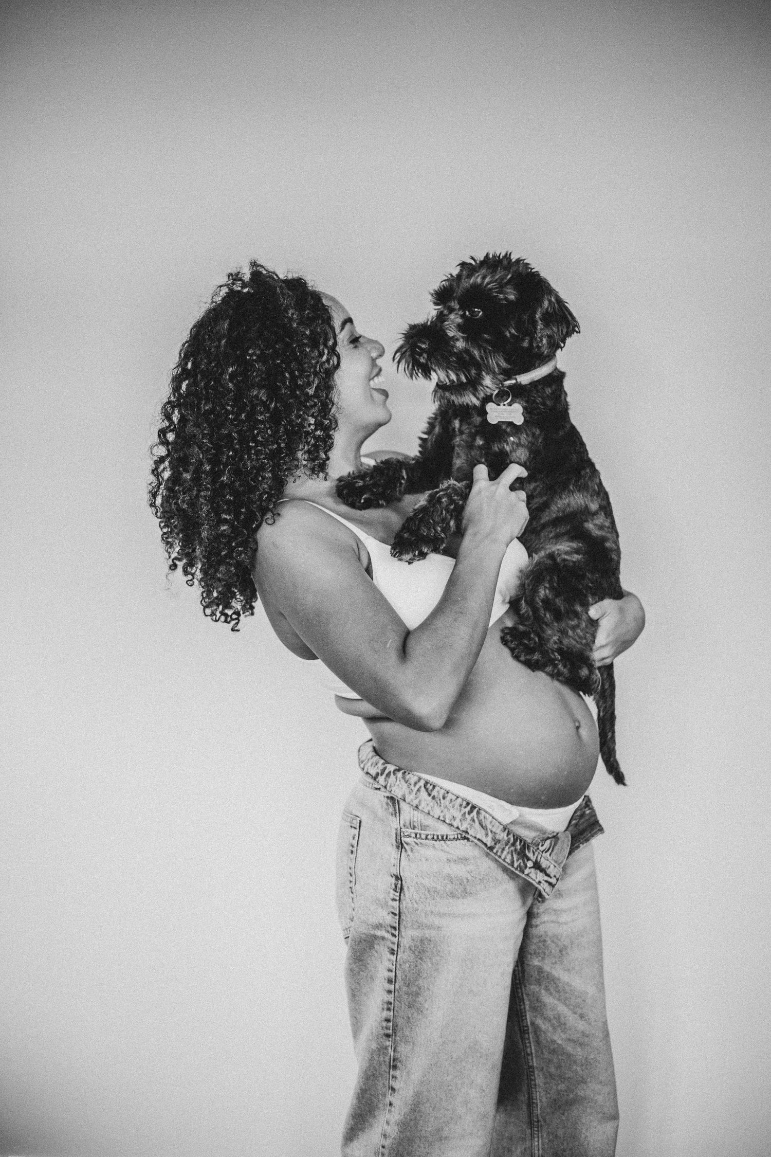 pregnant mother to be holding her dog on her bump and smiling during maternity shoot in Surrey with Dominique Lauren Photography