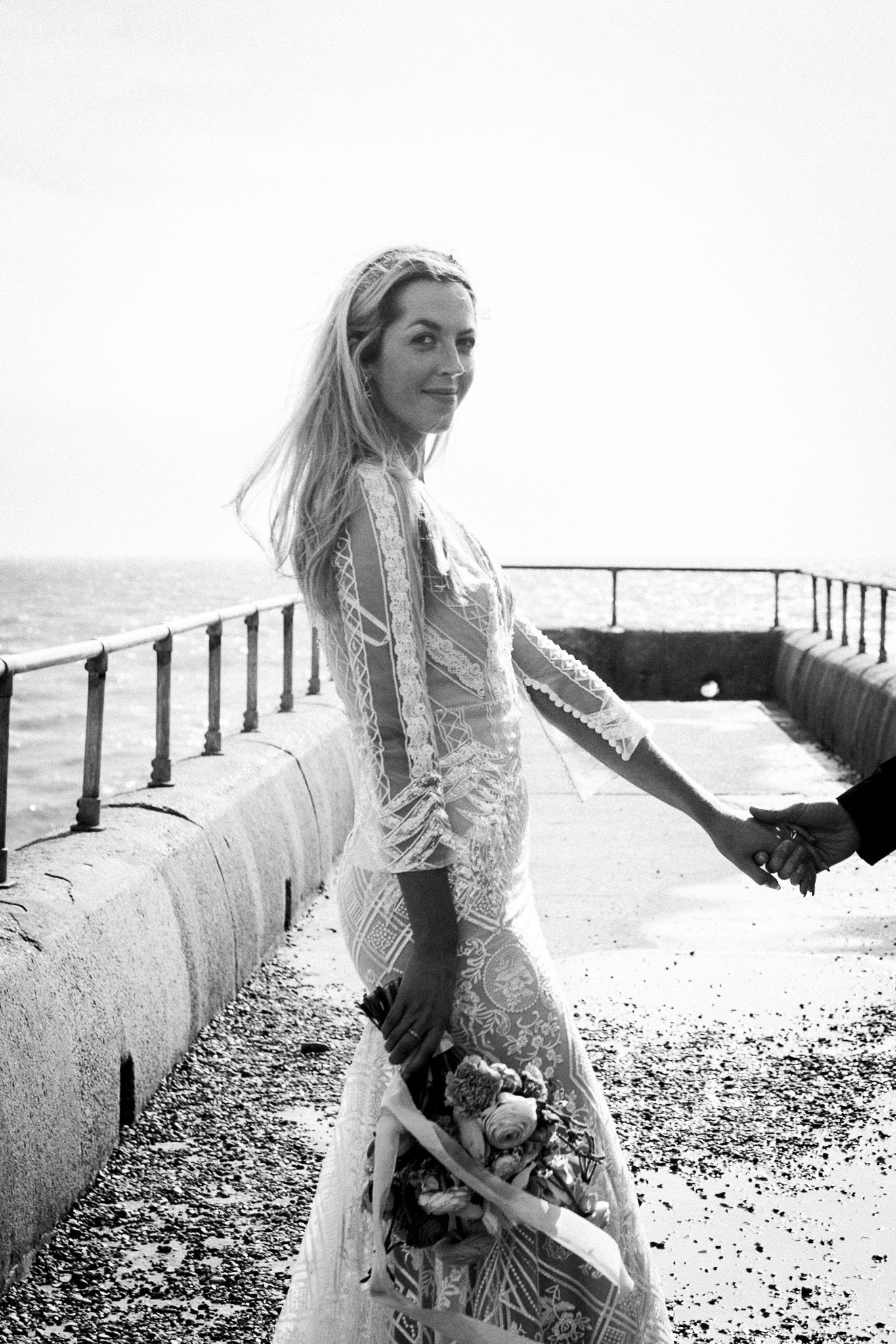 bride smiling on Brighton pier after elopement with groom, holding groom's hand who is out of shot