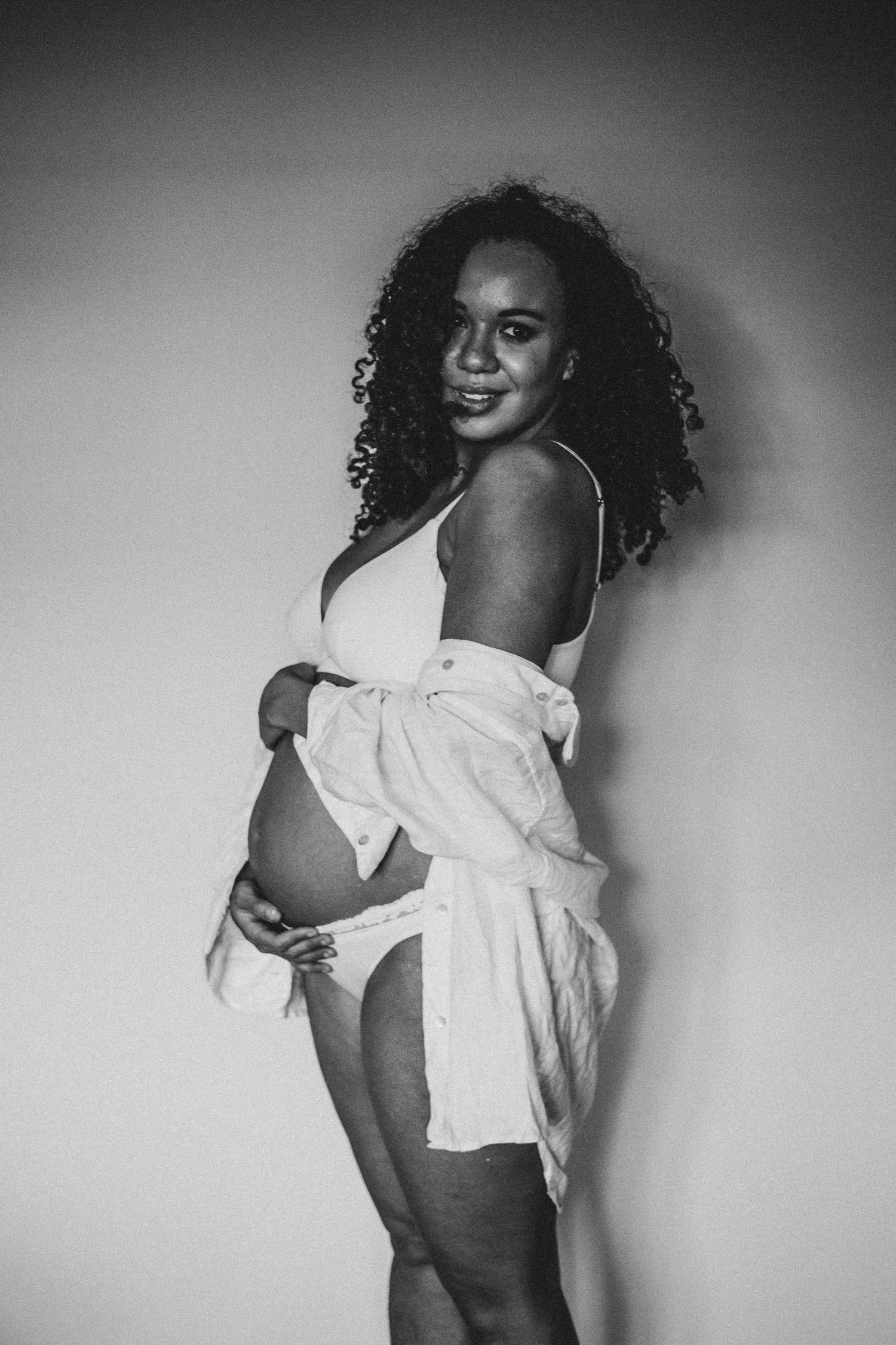 mother holding bump and looking directly into lens during maternity shoot in Surrey with Dominique Lauren Photography