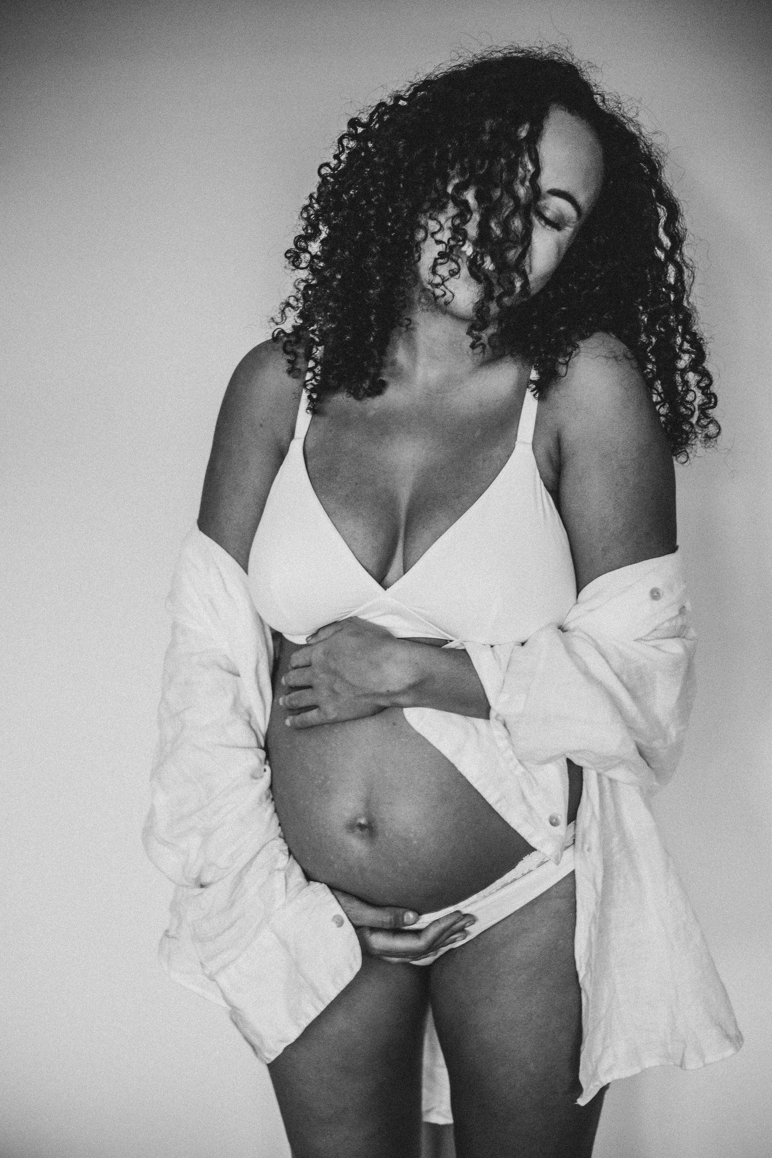 woman hugging bump and laughing in shirt and underwear during maternity shoot in Surrey with Dominique Lauren Photography