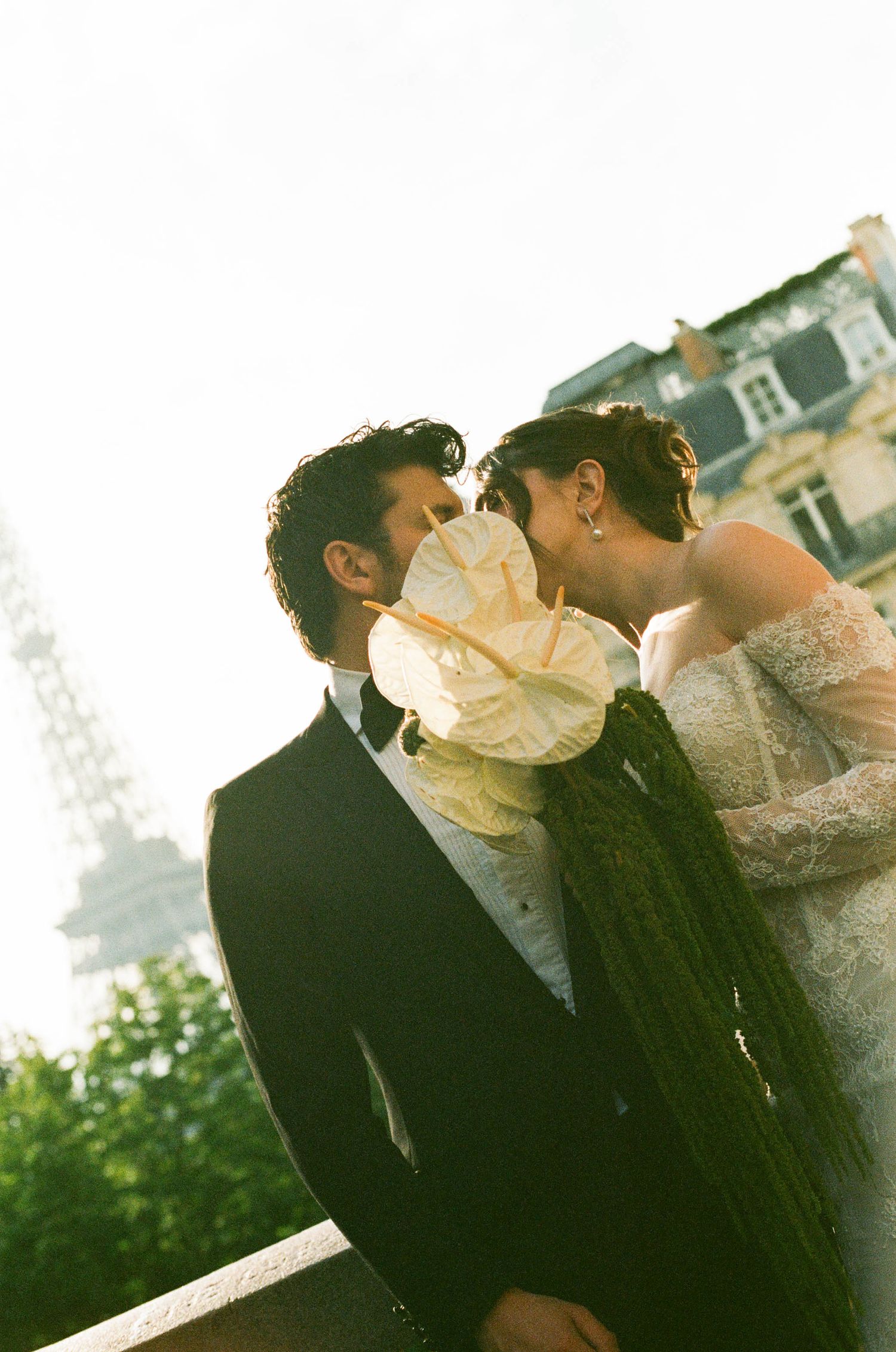 A romantic couple shares an intimate moment near the Eiffel Tower in Paris with soft sunlit lighting.