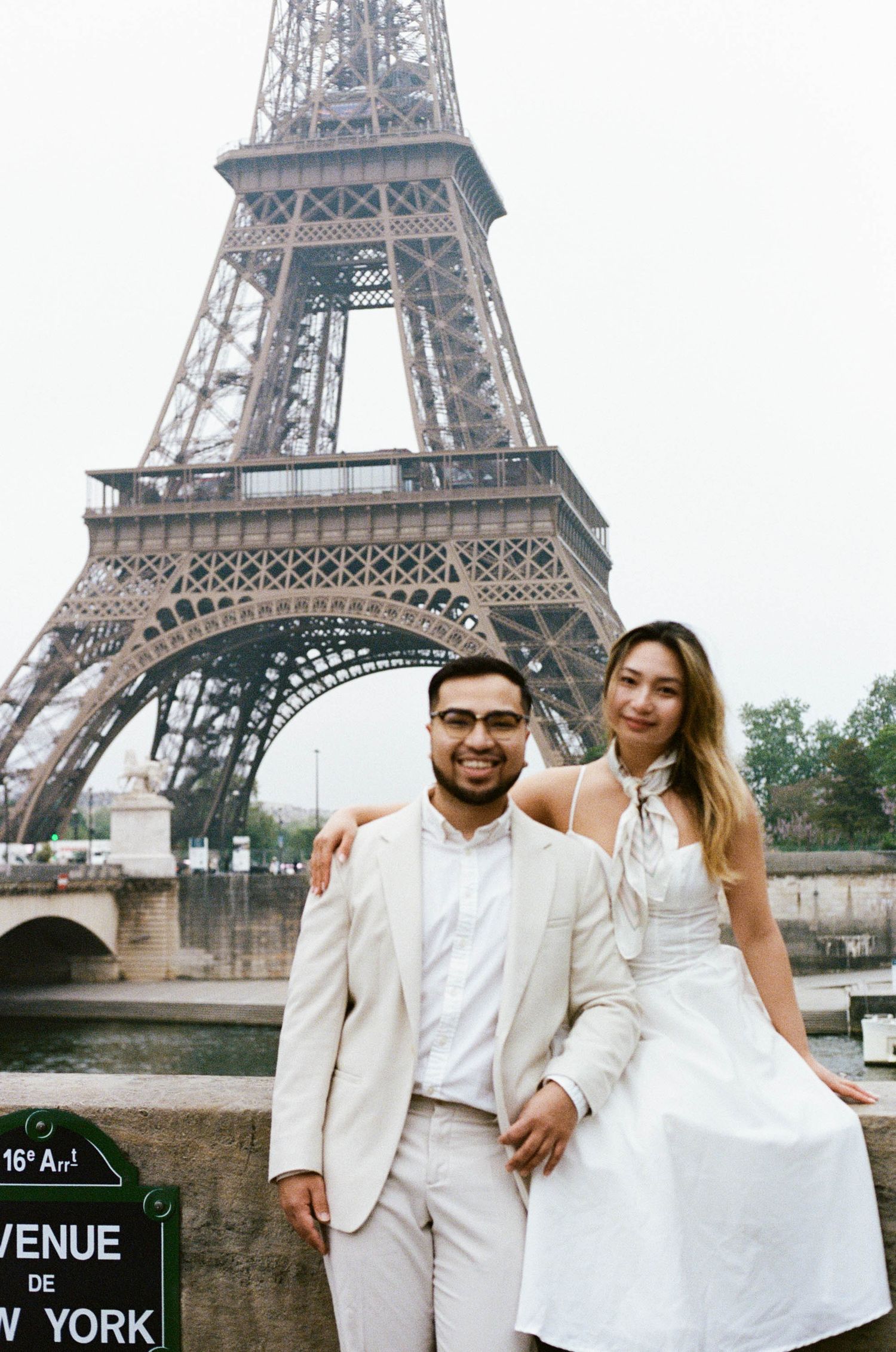 A couple in white attire pose together in front of the Eiffel Tower in Paris. Film photoshoot in Paris.