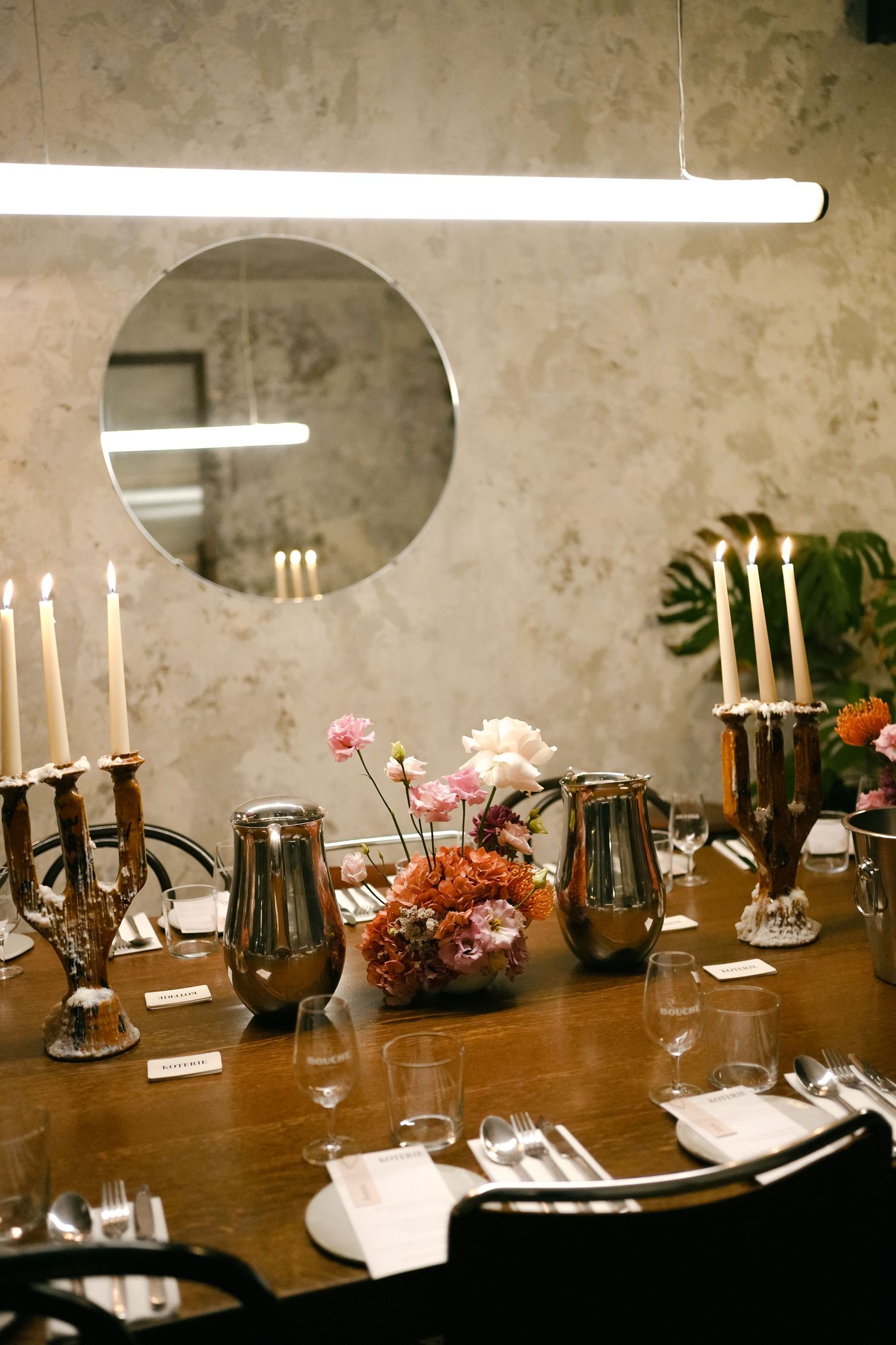 Long wooden dining table with candlesticks and decor set up for an elegant gathering in a moody, rustic setting.