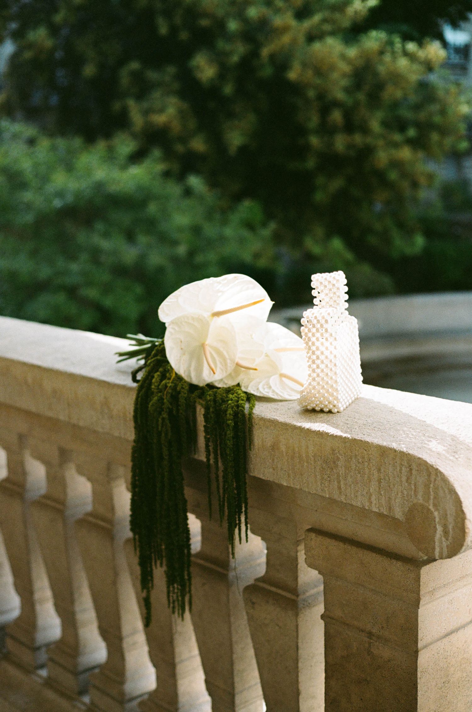 White origami paper decorations and dark greenery rest on a curved stone balustrade in an outdoor setting.