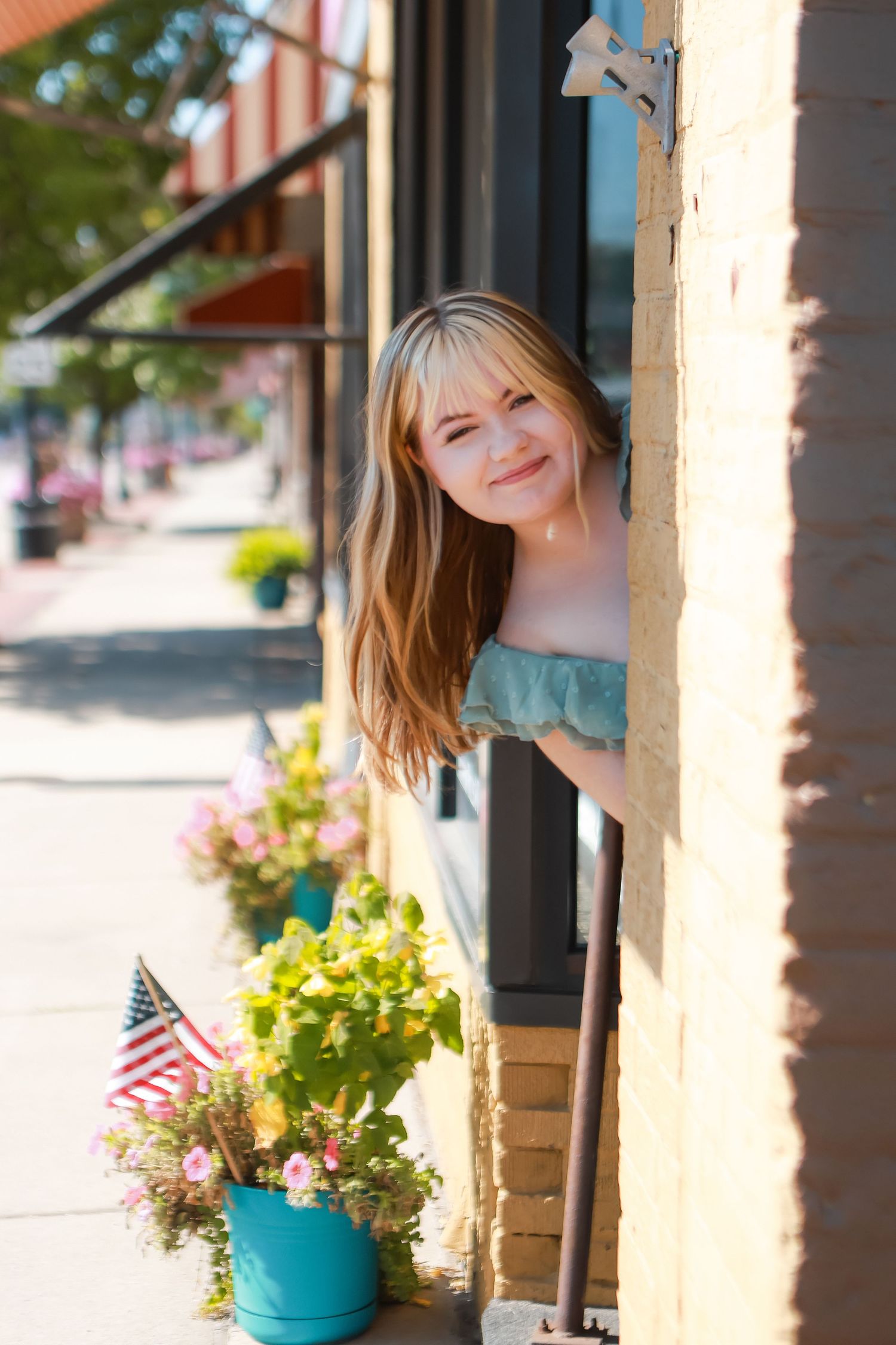 A bright turquoise flowerpot hangs on a porch column with an American flag visible in the background.