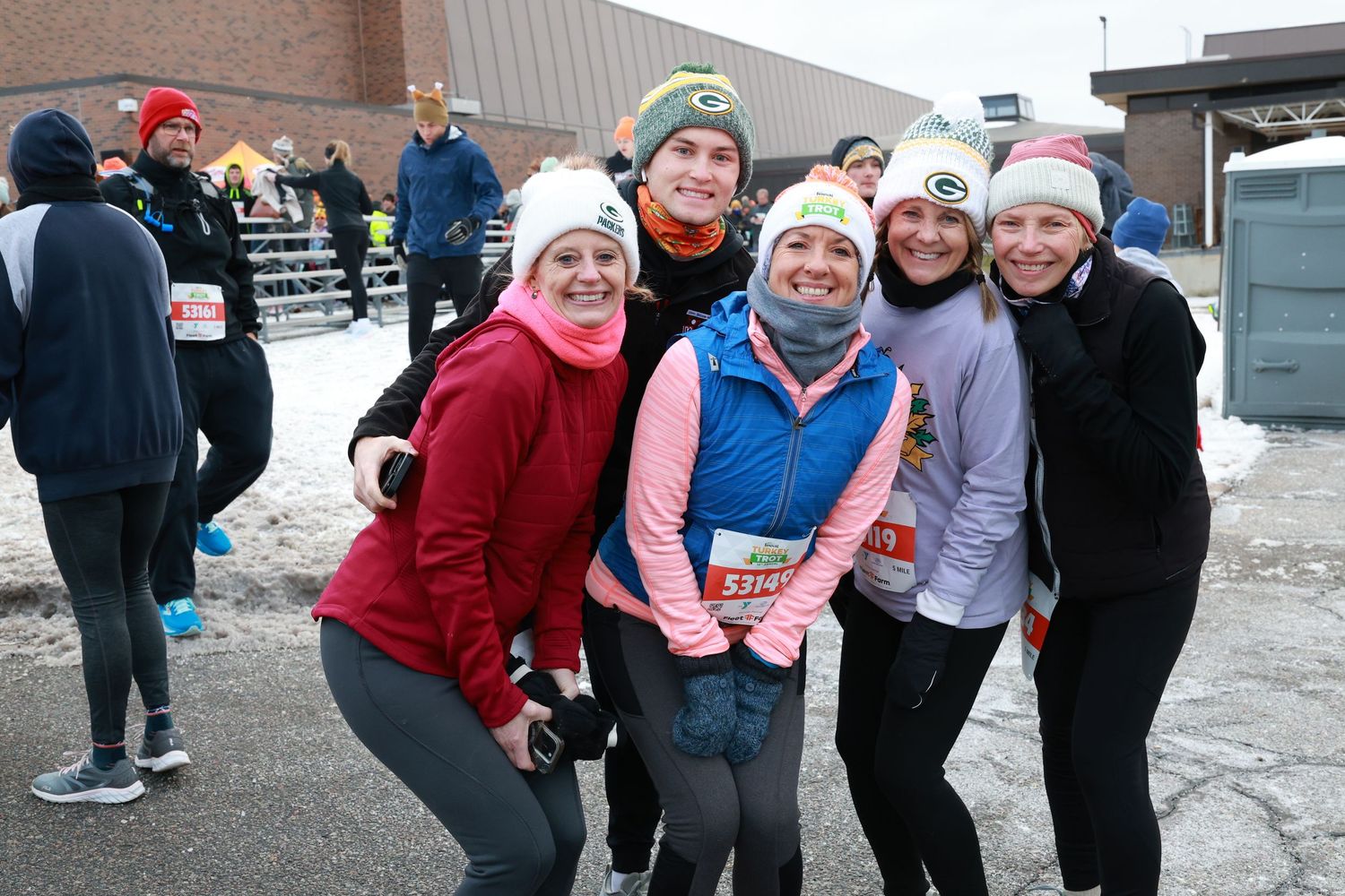 A group of runners bundled up in winter gear pose together at an outdoor winter race event.
