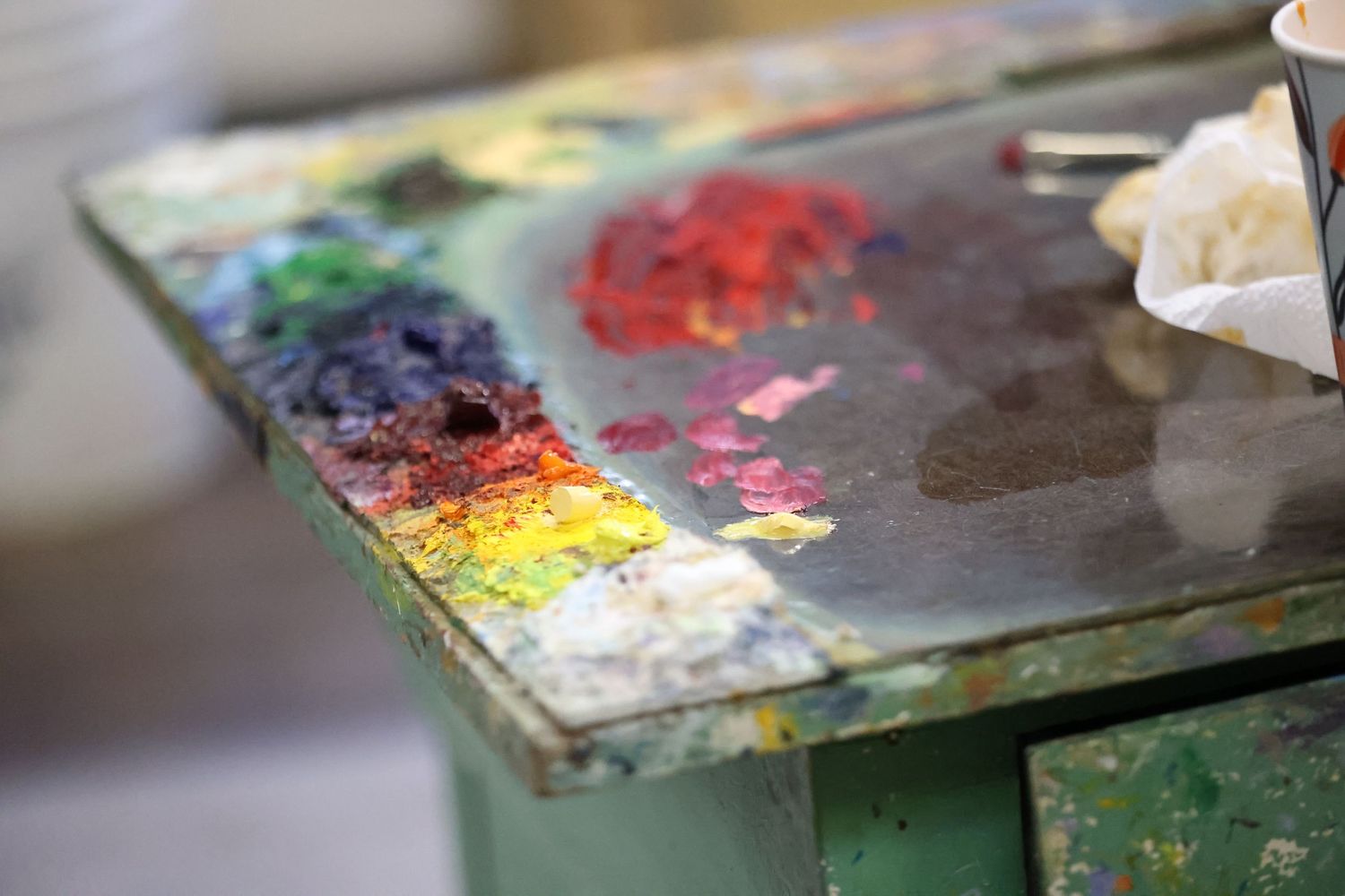 Close-up view of colorful artist paint palettes with mixed oil paints and brushes on a wooden surface.