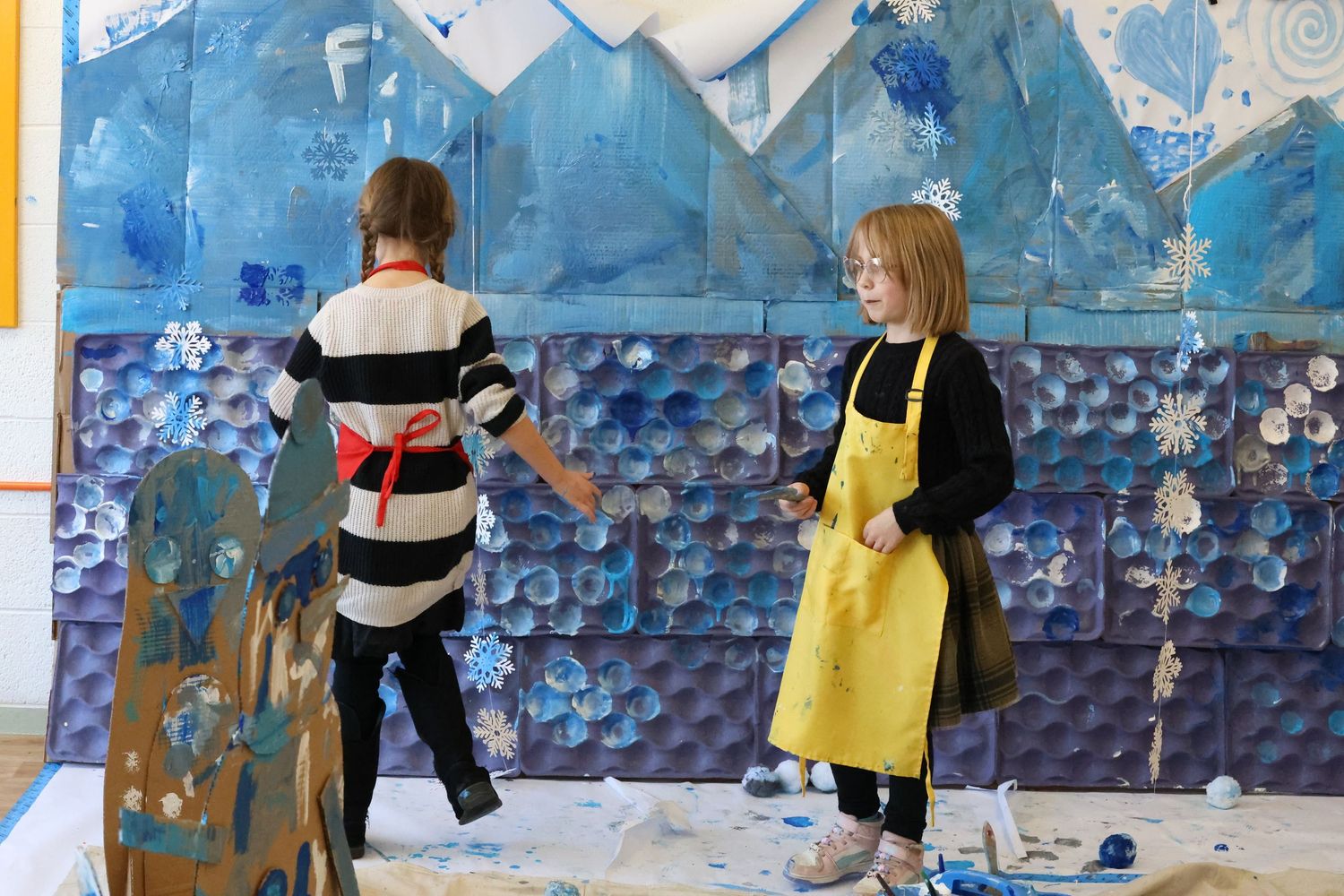 Rock climbers scale a blue indoor climbing wall with various colored holds and routes marked on its surface.